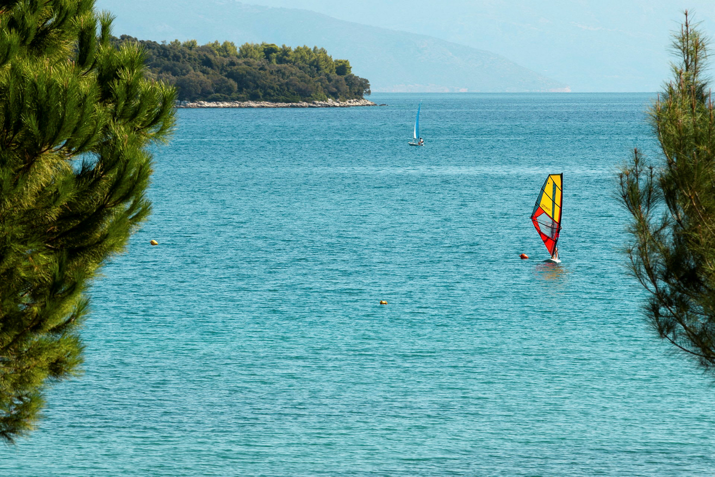 Windsurfer med fargerik seil på havet, omgitt av grønt. (AI-generert tekst)