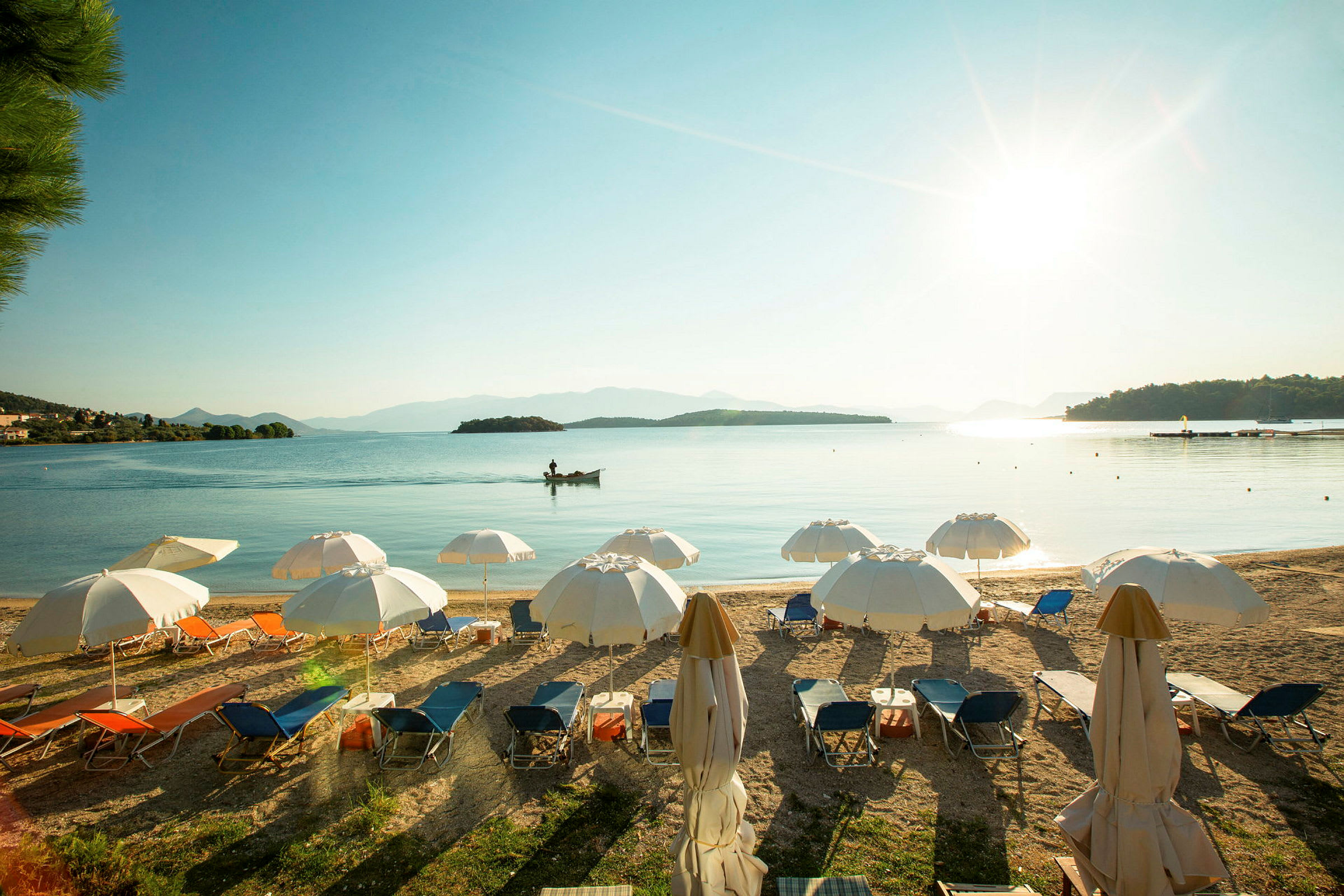 Strand med solsenger og parasoller, med havet og små øyer i bakgrunnen under en klar himmel. (AI-generert tekst)