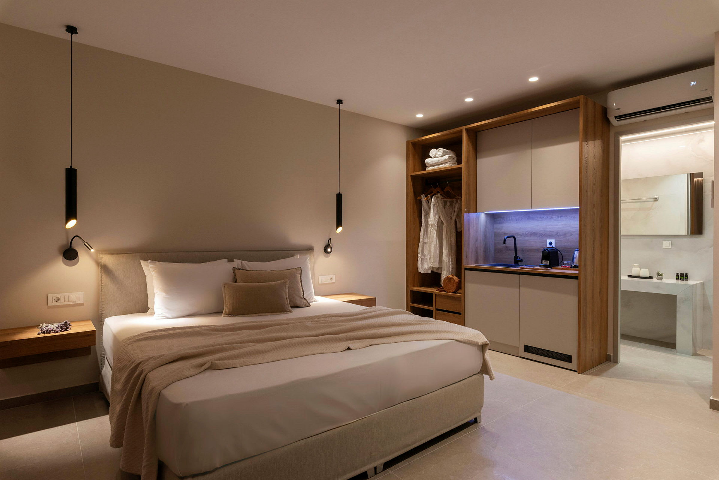 Moderne innredet hotellrom med stor seng, garderobe og kjøkkenkrok, samt inngang til bad. (AI-generert tekst)