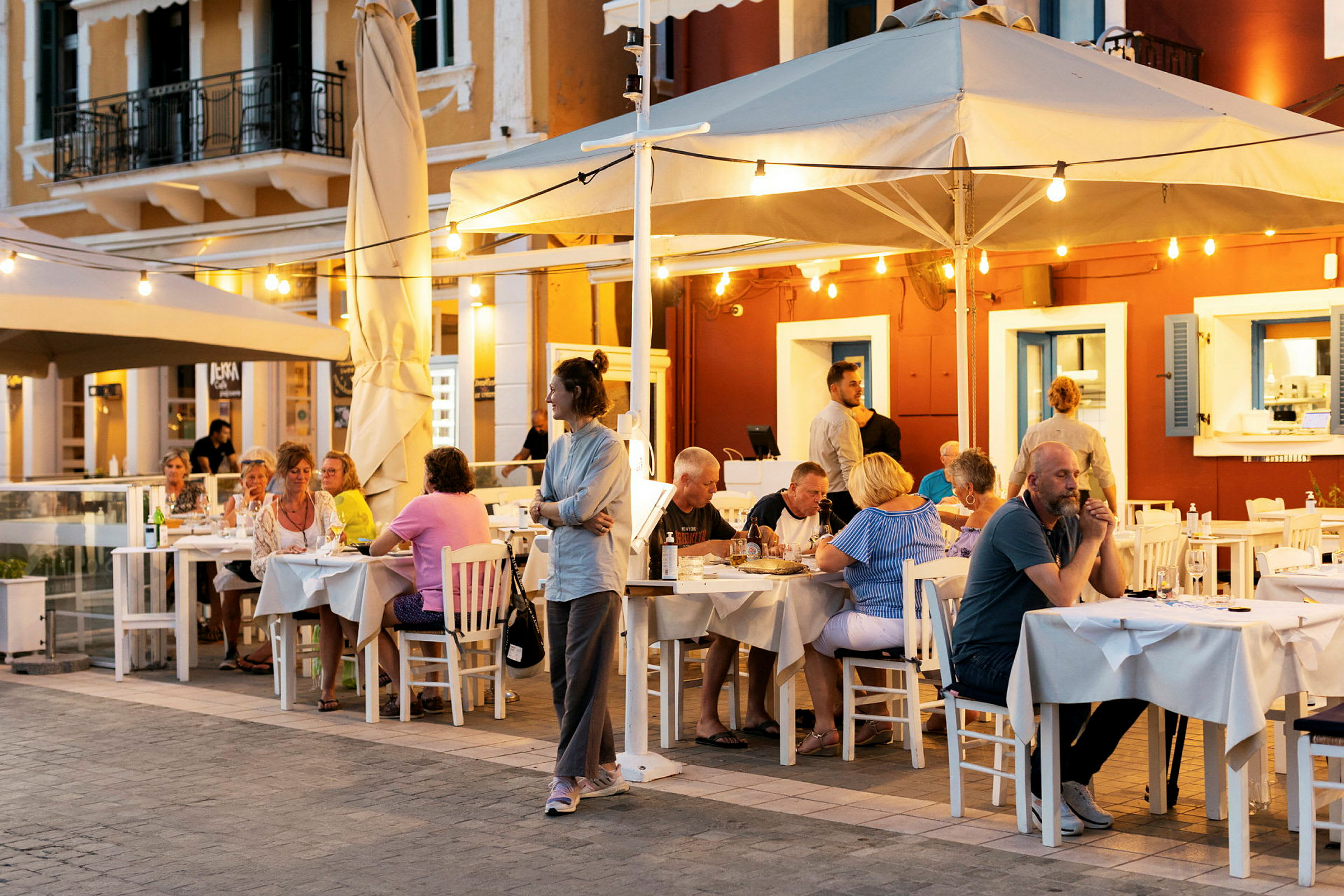 Utendørsrestaurant med gjester sittende ved bord på kveldstid. (AI-generert tekst)