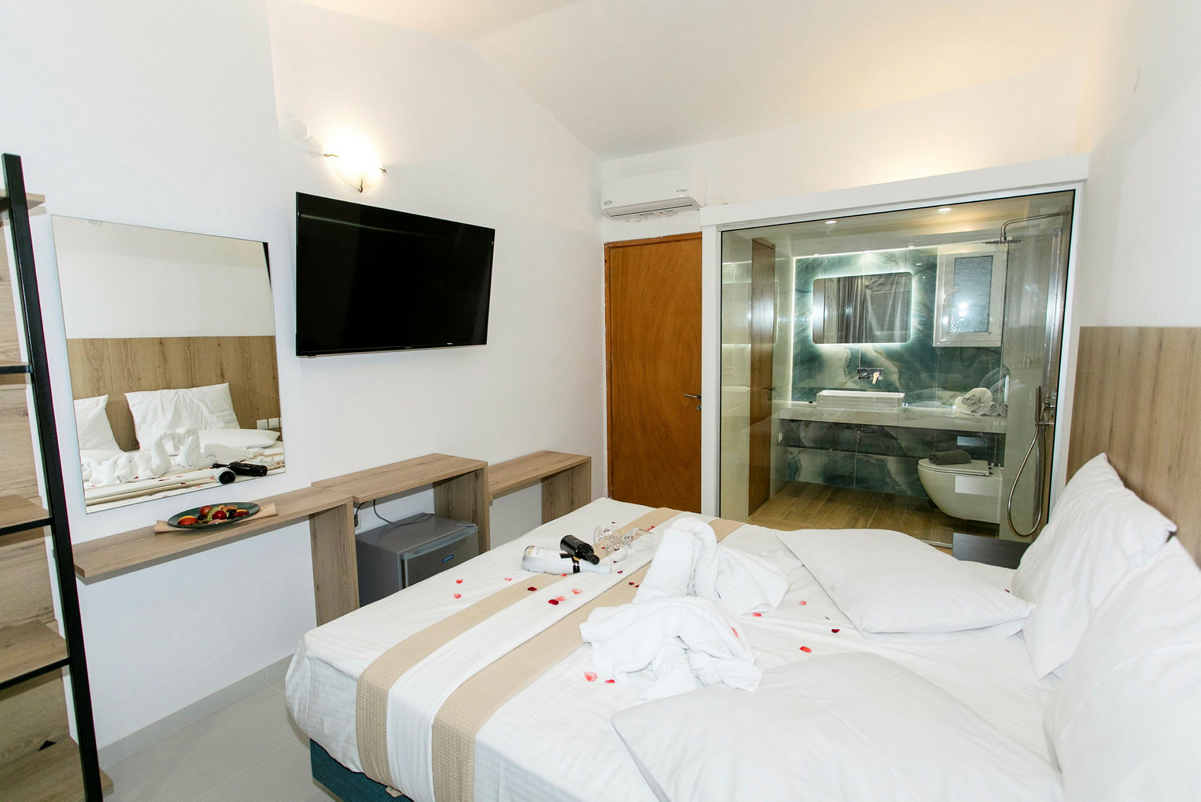 Hotellrom med en stor seng, et åpent bad med glassvegg og en møblering inkludert en TV. (AI-generert tekst)