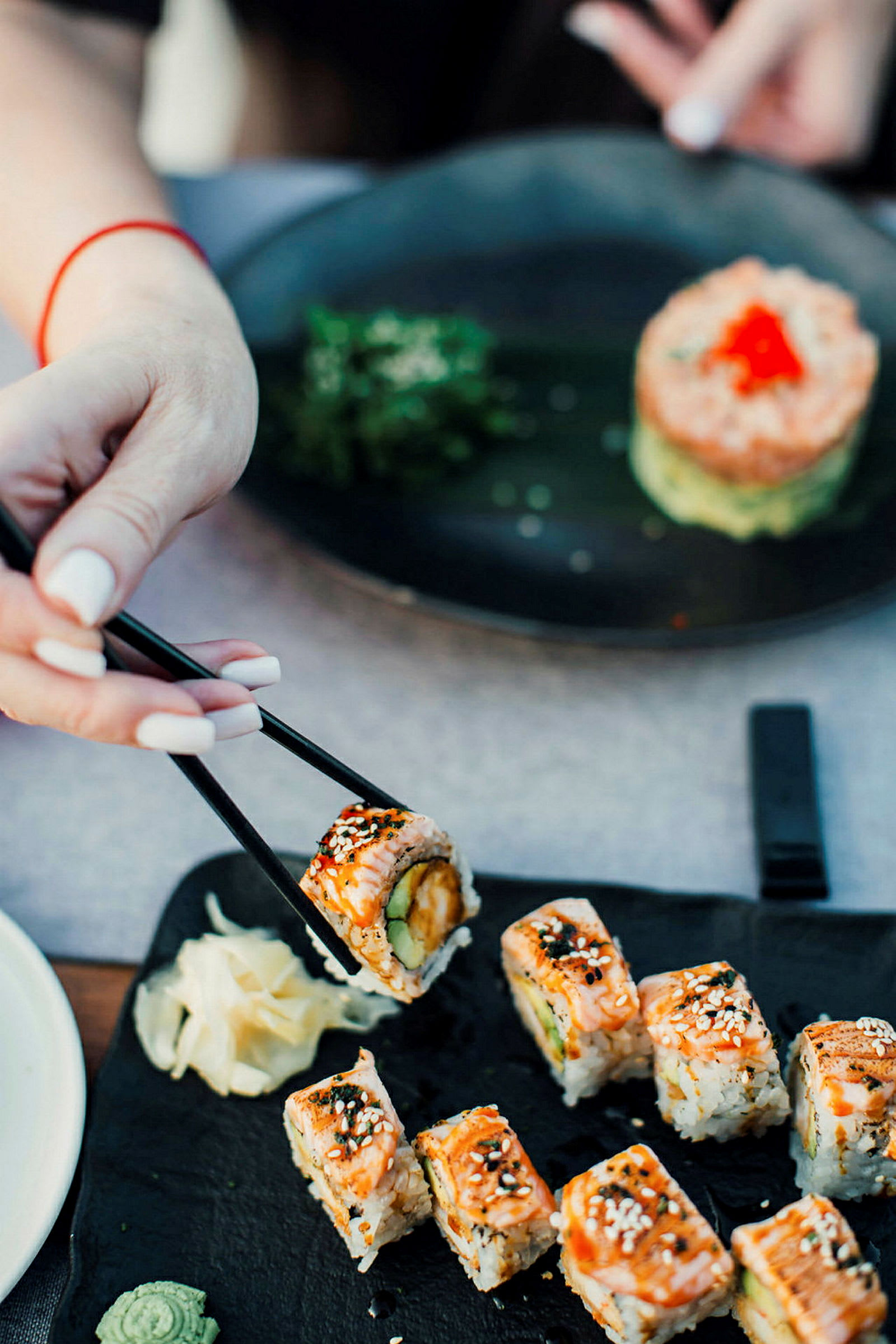 Sushi servert på en svart tallerken, med en hånd som holder en bit med spisepinner. (AI-generert tekst)