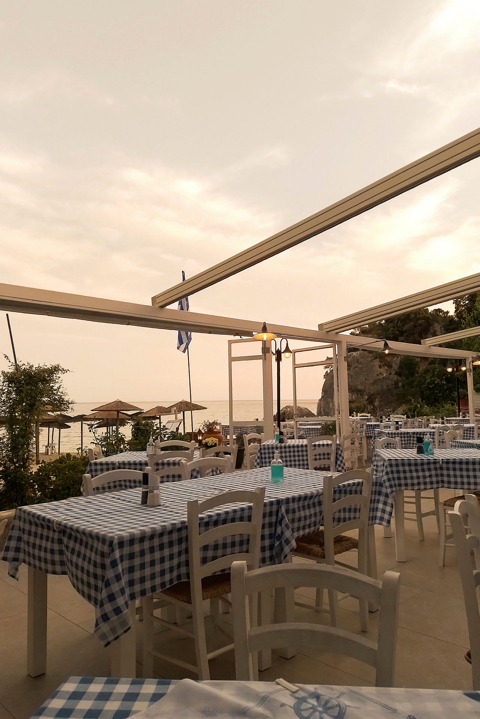 Restaurant med rutete duker og utsikt mot havet under en skyet himmel. (AI-generert tekst)