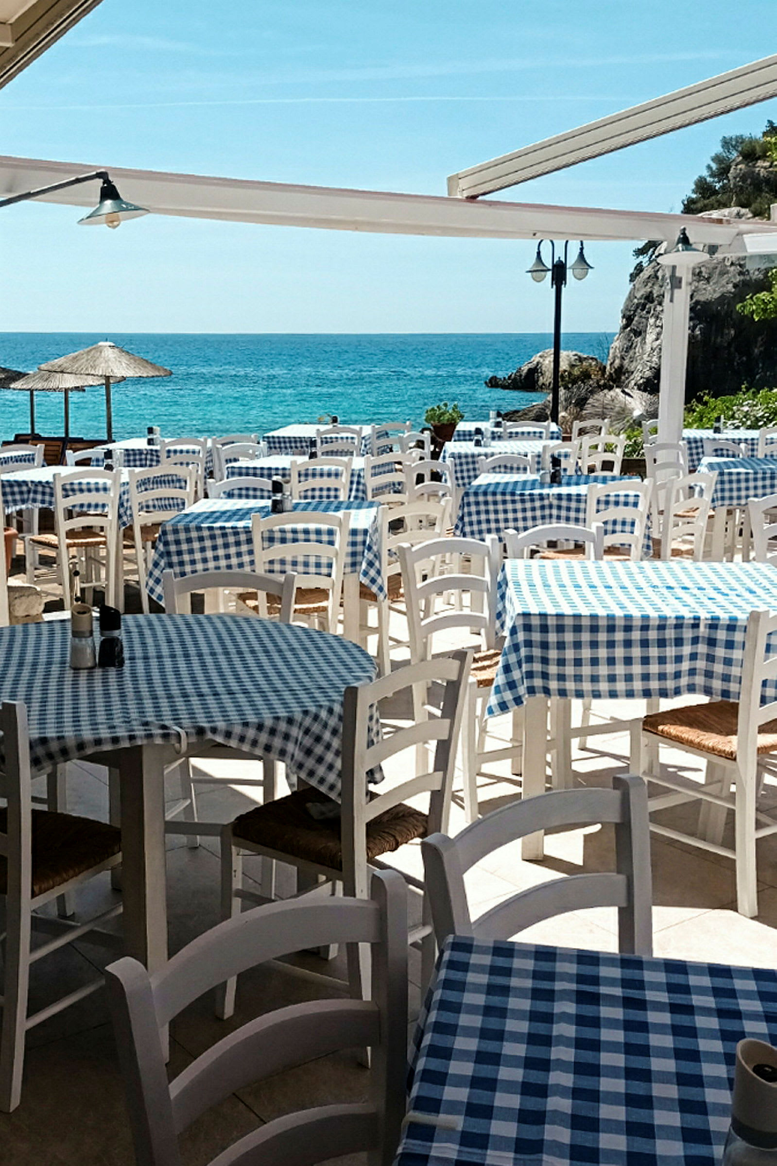 Restaurant ved havet med dekkede bord og stoler utendørs. (AI-generert tekst)