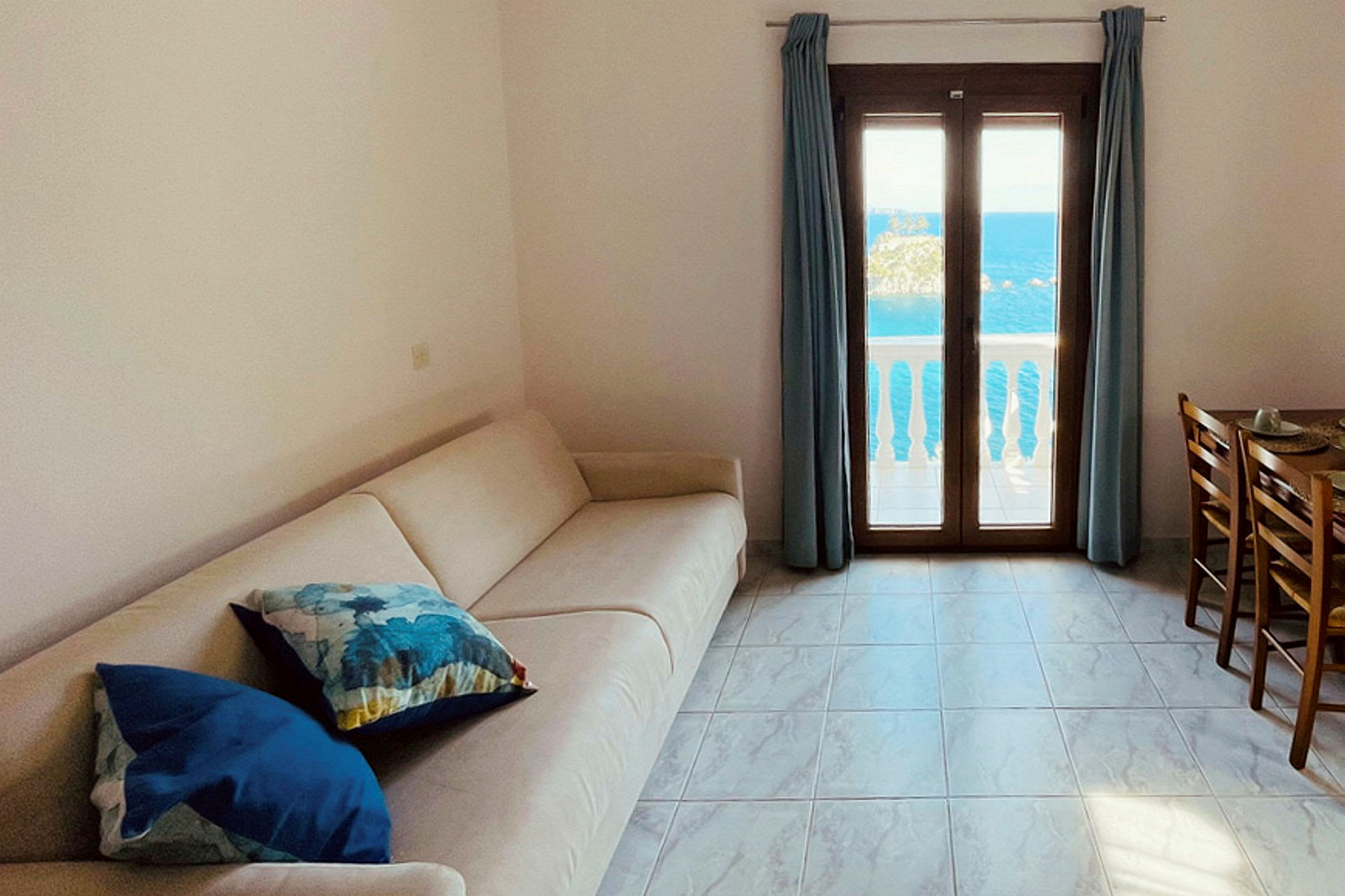 En stue med en sofa, et spisebord og en balkong med utsikt over havet. (AI-generert tekst)