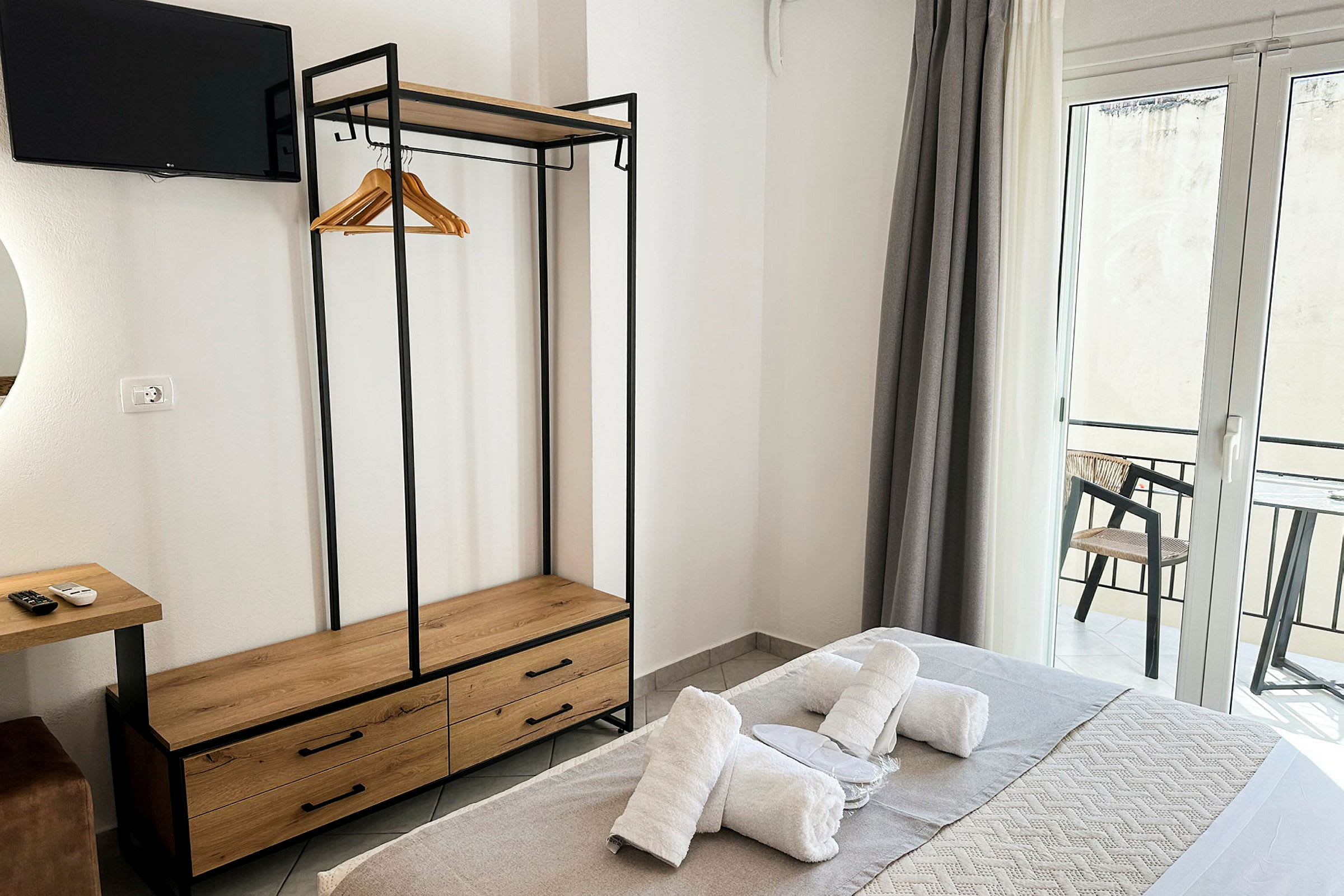 Et hotellrom med seng utstyrt med håndklær, garderobe med kleshengere, TV og balkong med utsikt. (AI-generert tekst)