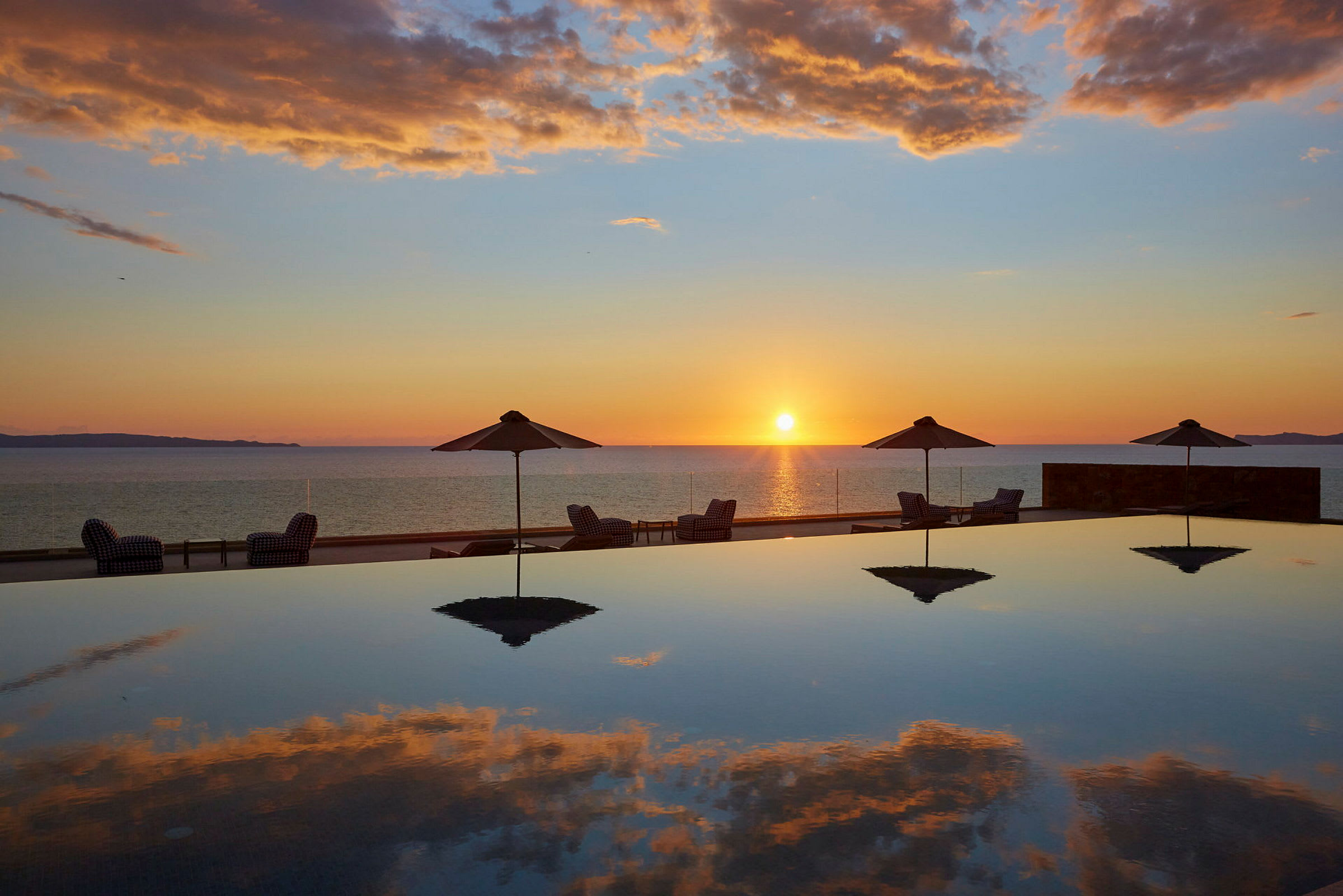 Solnedgang over havet med parasoller og solsenger ved et basseng. (AI-generert tekst)