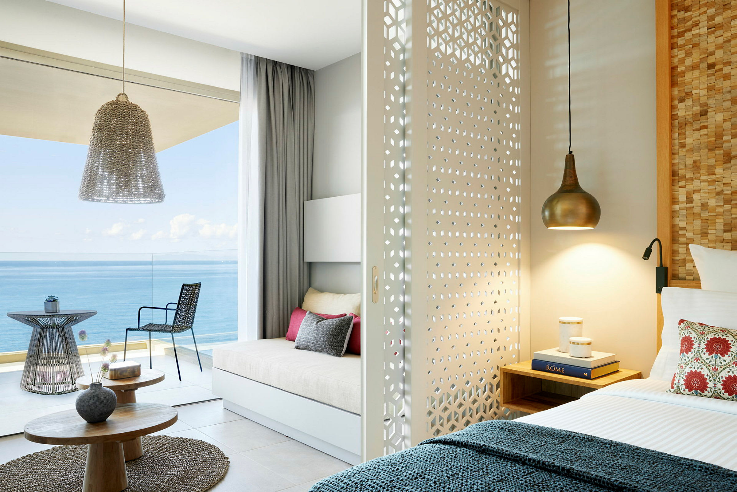 Et lyst hotellrom med en skyvbar dekorert skillevegg, seng og sittegruppe med utsikt over havet. (AI-generert tekst)
