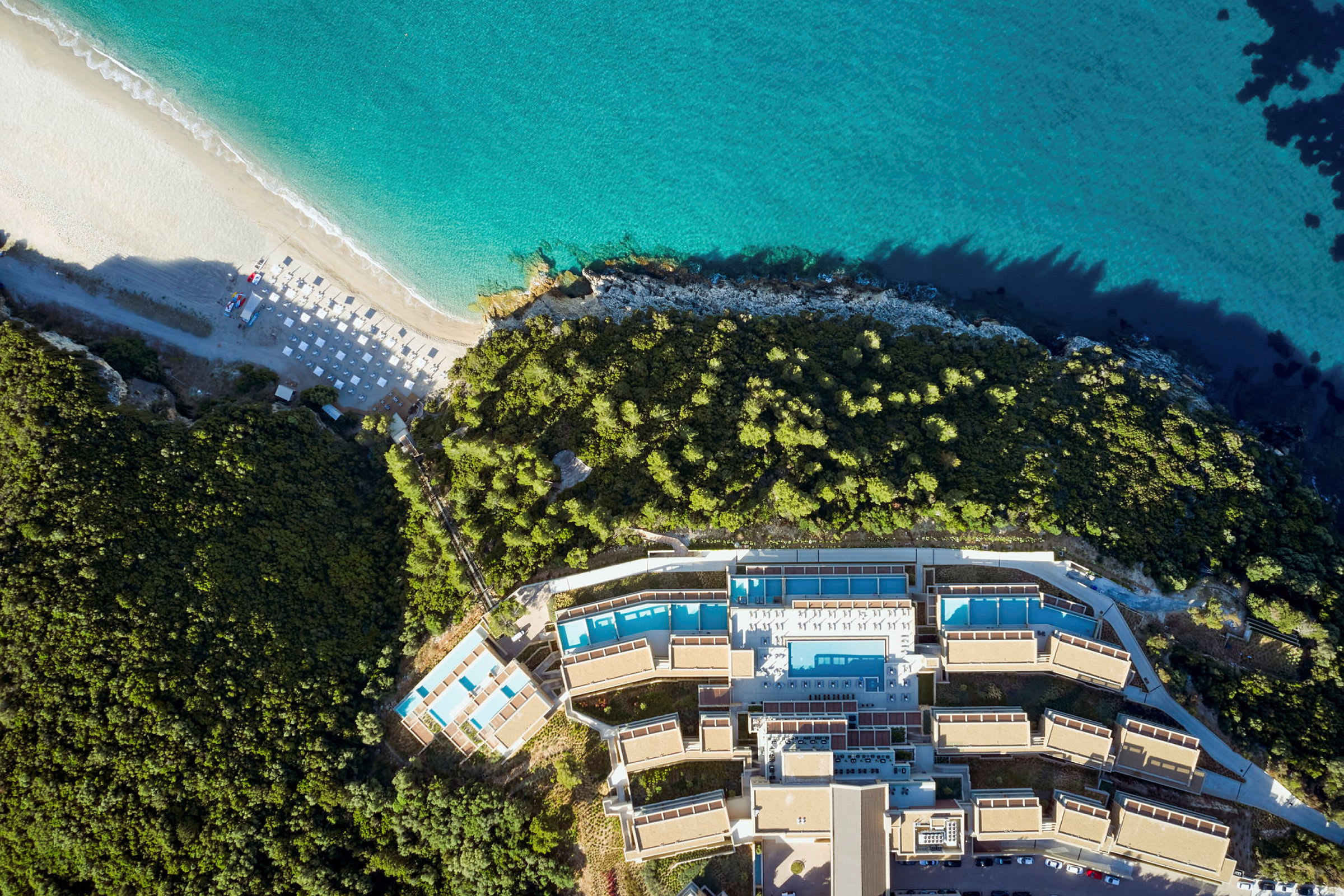Flyfoto av et hotellkompleks ved stranden med omkringliggende vegetasjon. (AI-generert tekst)