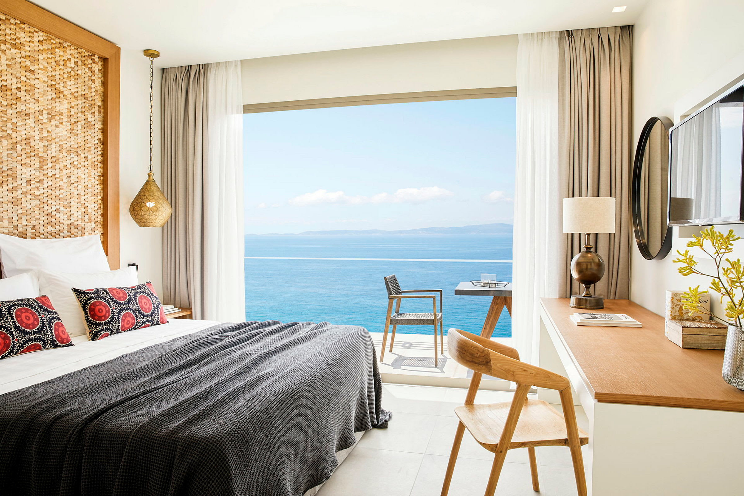 Et hotellrom med en oppredd seng, skrivebord og utsikt over havet gjennom vinduet. (AI-generert tekst)