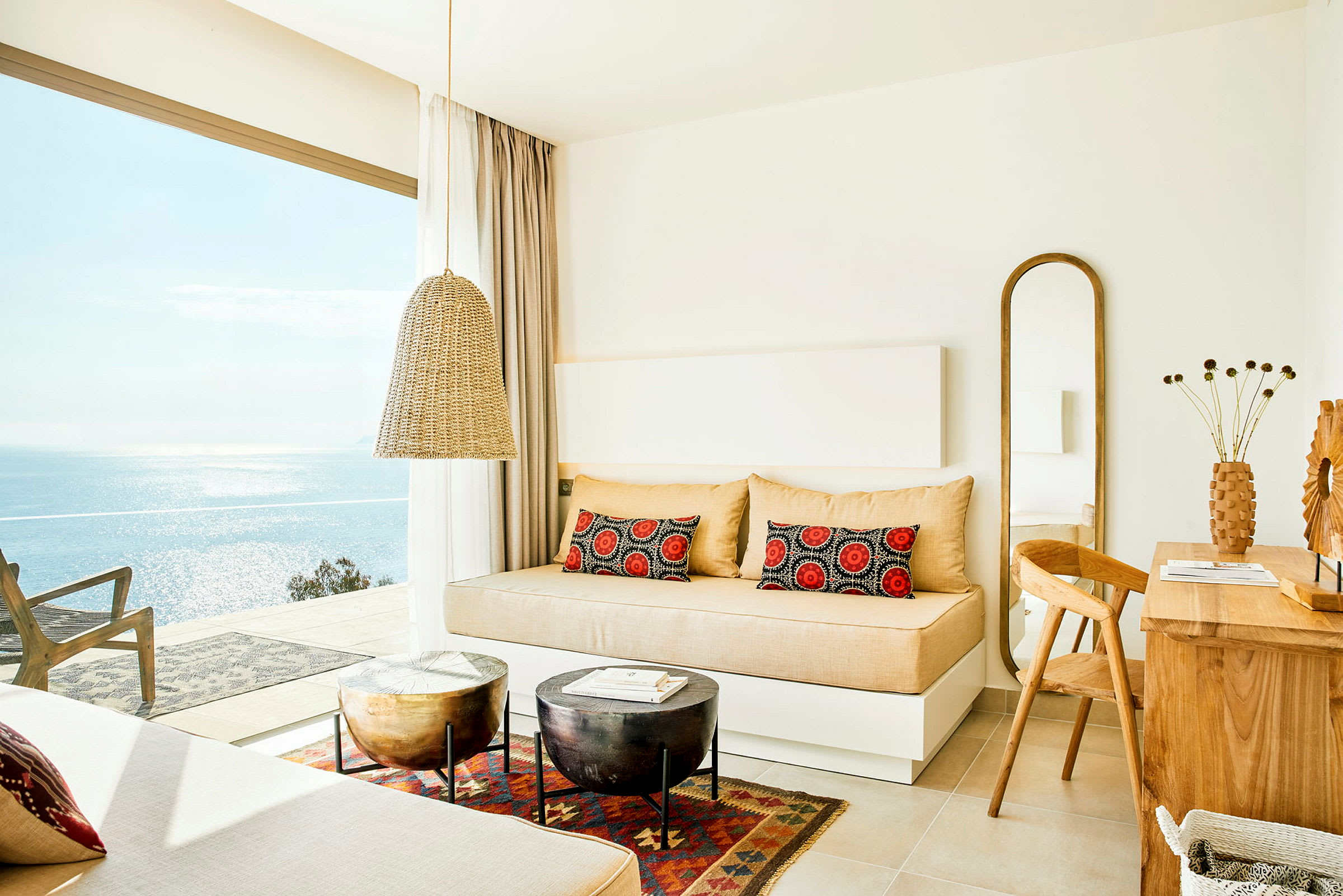 Lyst hotellrom med sovesofa, trebord og havutsikt gjennom store vinduer. (AI-generert tekst)