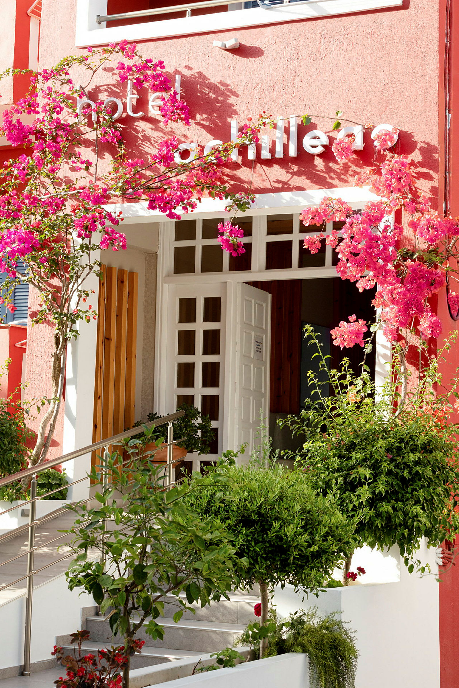 Inngang til hotell med hvite dører og rosa blomster. (AI-generert tekst)