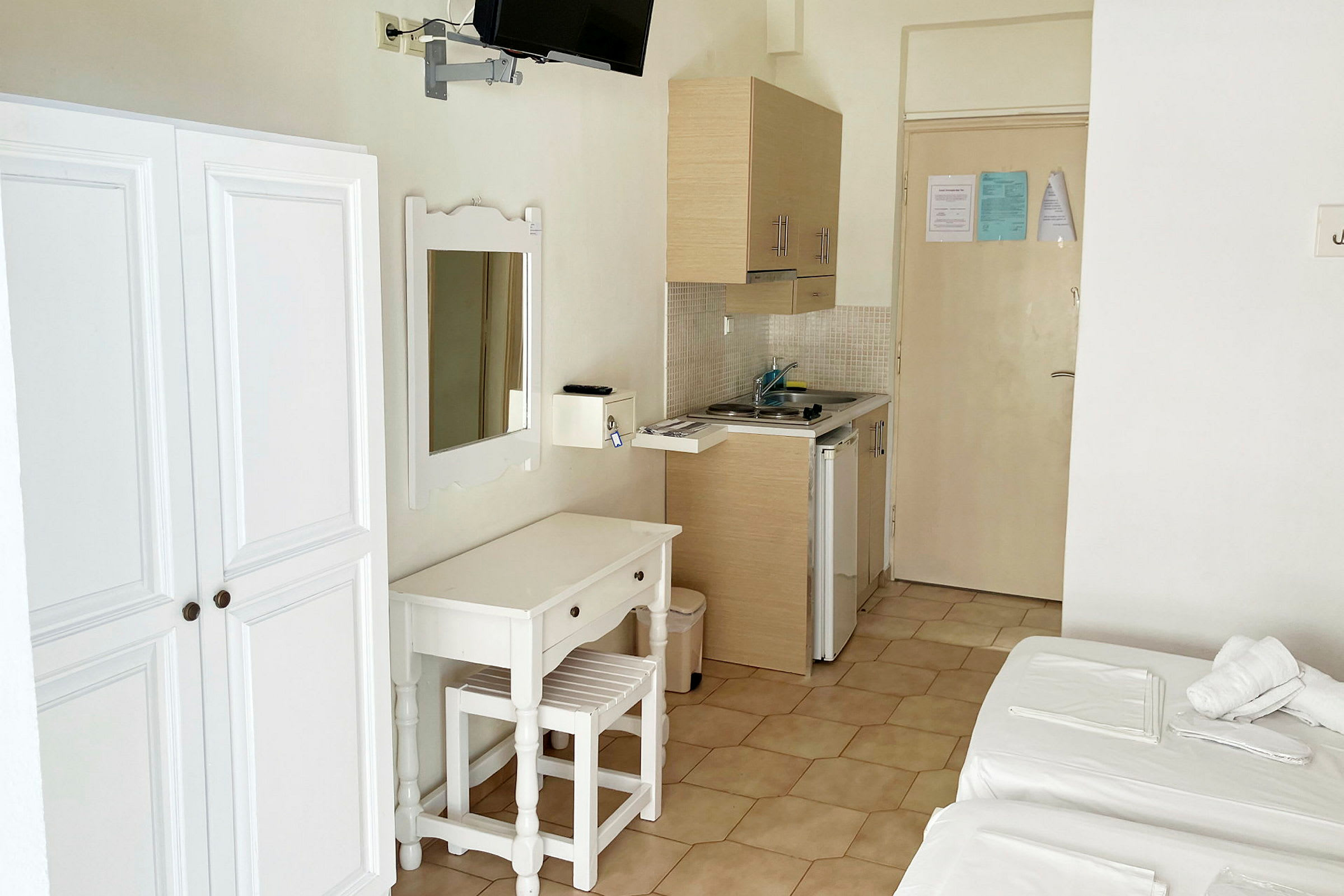 Bilde av et hotellrom med garderobeskap, speil, skrivebord med stol og en liten kjøkkenkrok med vask. (AI-generert tekst)