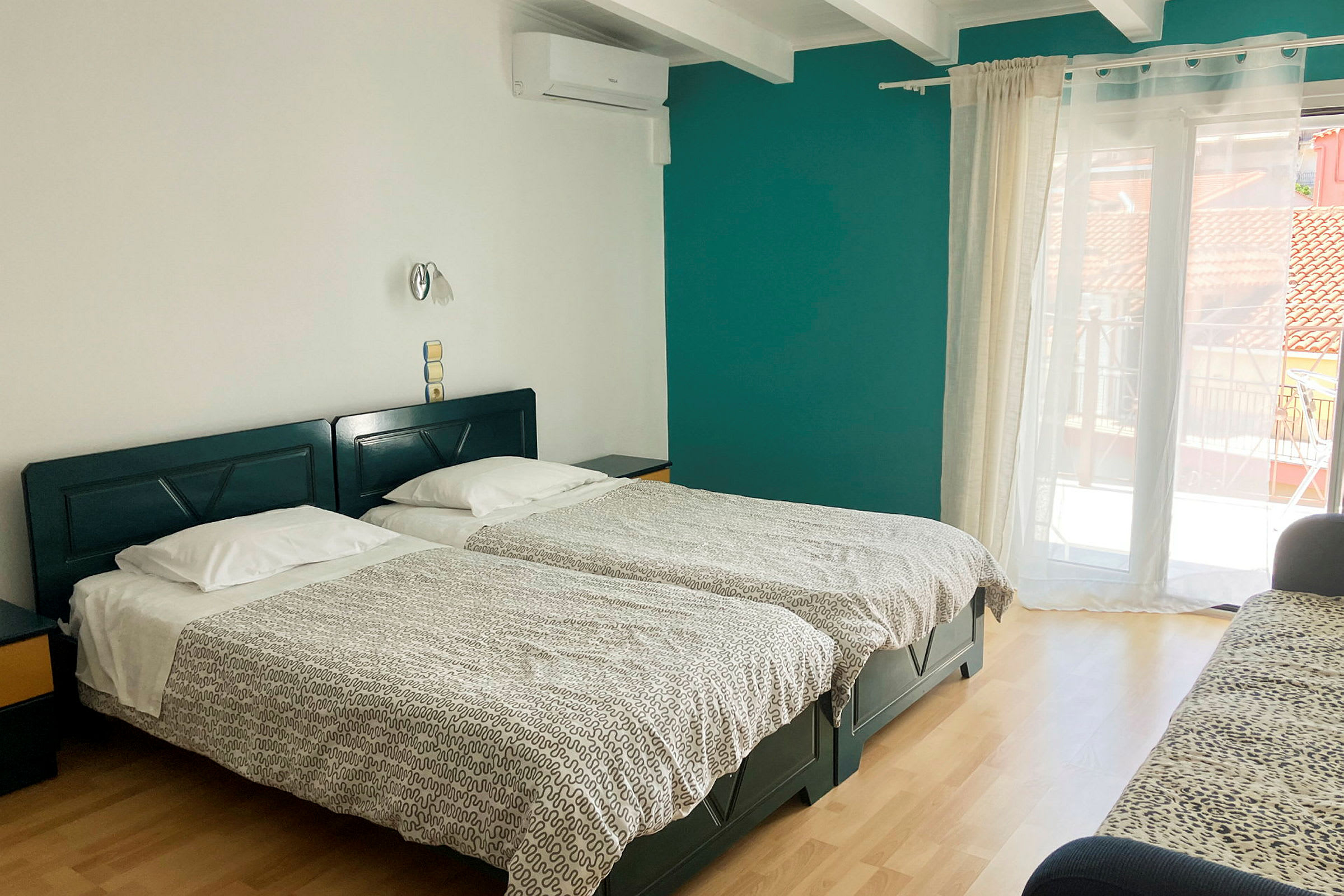 Et hotellrom med to enkeltsenger, en sofa og en balkongdør. (AI-generert tekst)