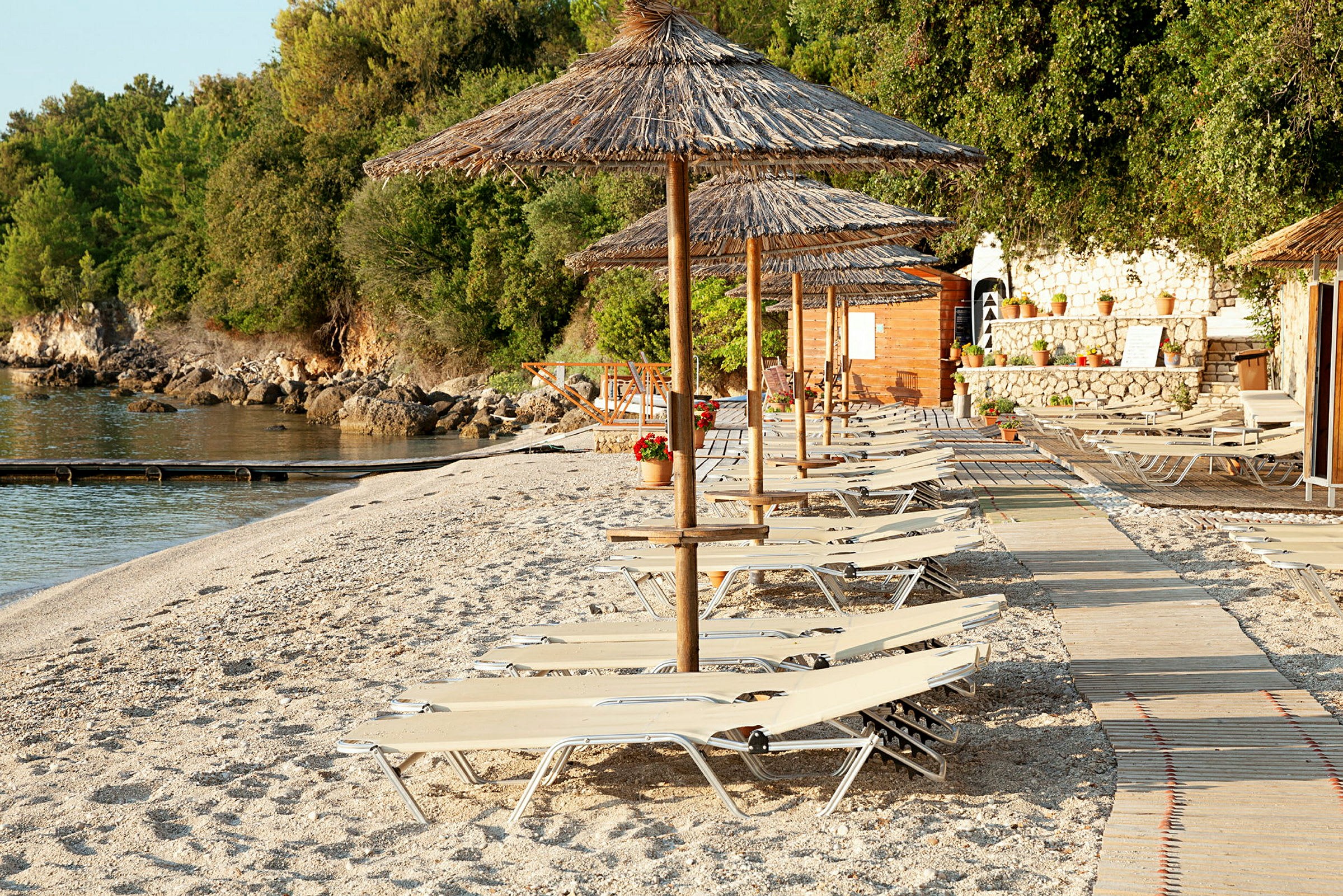 Solstoler og parasoller på en strand med en tresti og grøntområder i bakgrunnen. (AI-generert tekst)