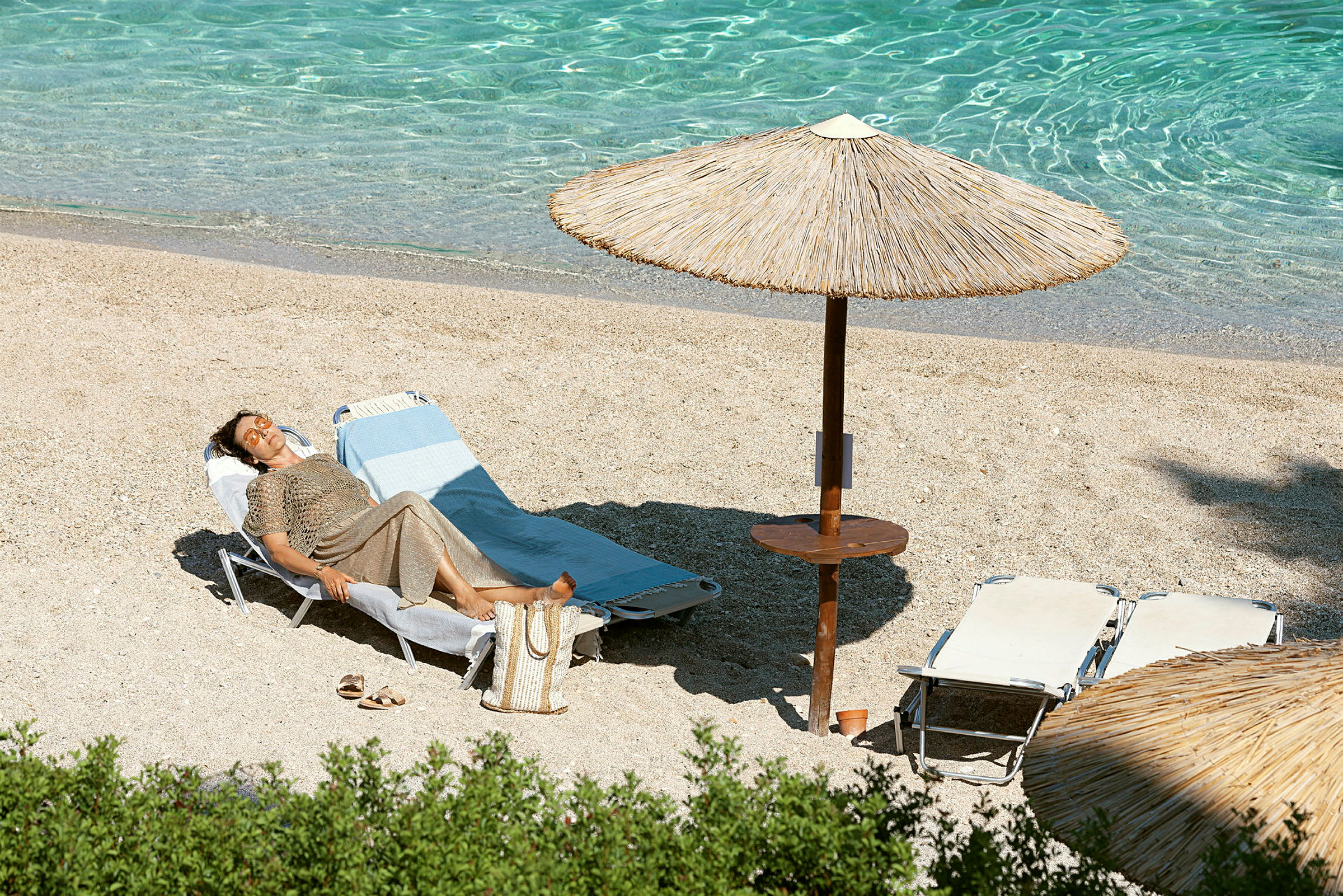 En person ligger på en solseng på stranden under en parasoll ved siden av klart vann. (AI-generert tekst)