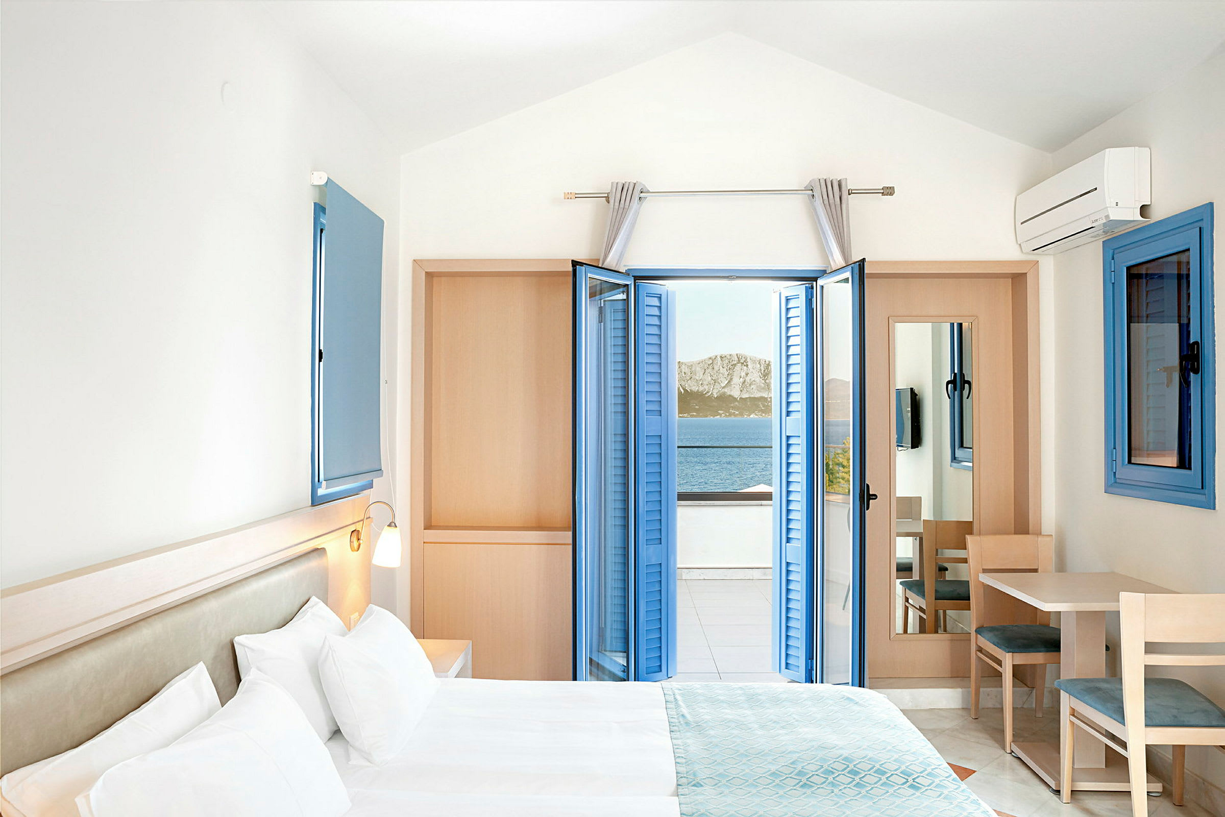Hotellrom med dobbeltseng og havutsikt gjennom åpne blå vinduslemmer. (AI-generert tekst)