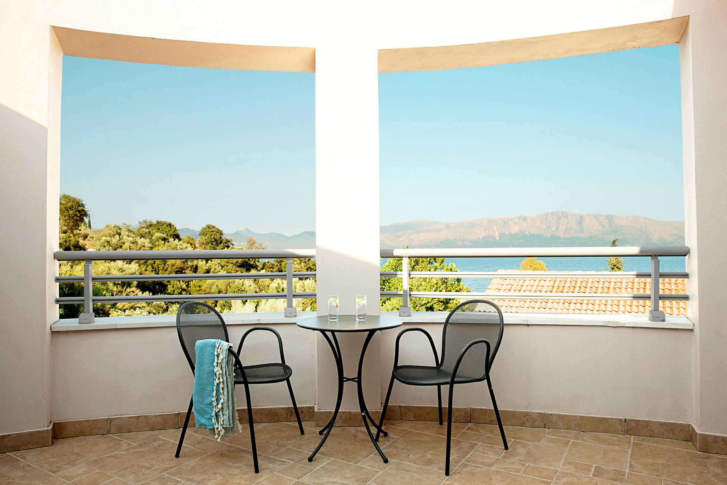 Terrasse med to stoler og et bord, utsikt over havet og det omkringliggende landskapet. (AI-generert tekst)