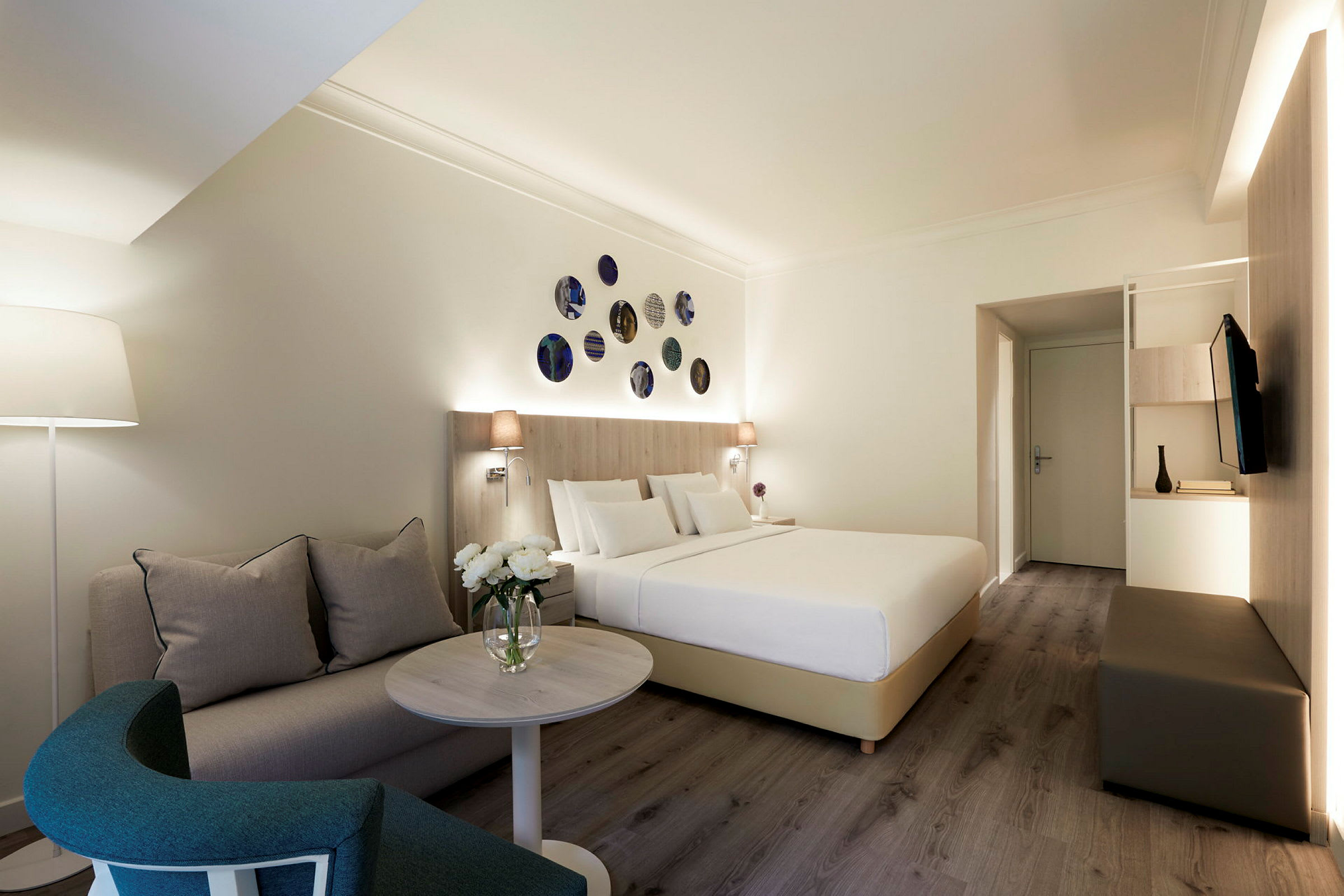 Et hotellrom med en seng, en sofa og et salongbord, dekorert med moderne detaljer. (AI-generert tekst)
