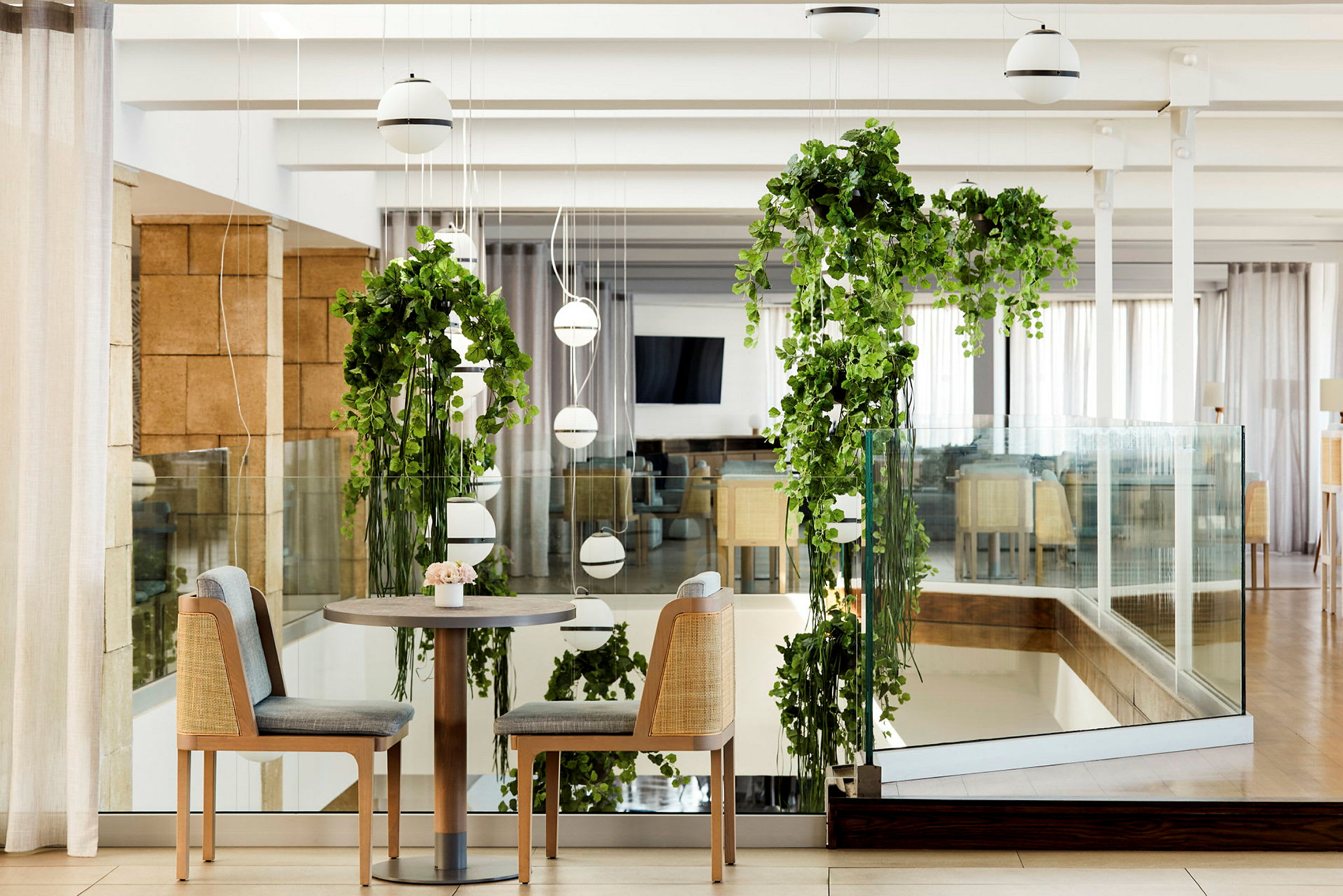 Et par stoler ved et bord, omgitt av hengende grønne planter og moderne interiør. (AI-generert tekst)