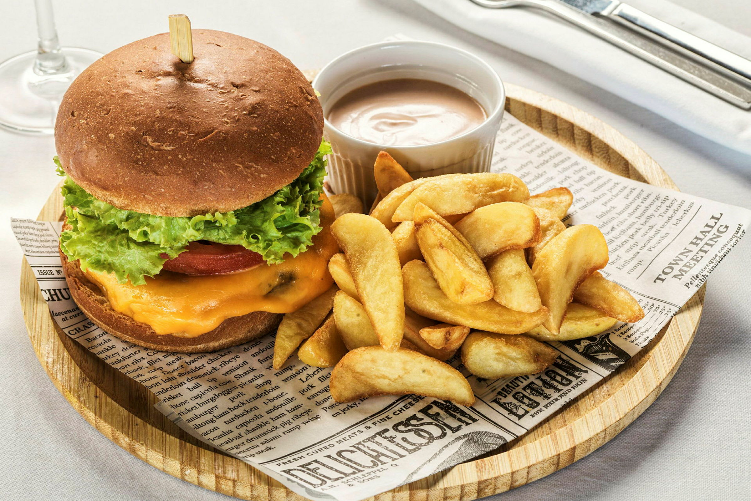 En hamburger med salat, tomat og ost servert med potetbåter og en dippsaus. (AI-generert tekst)