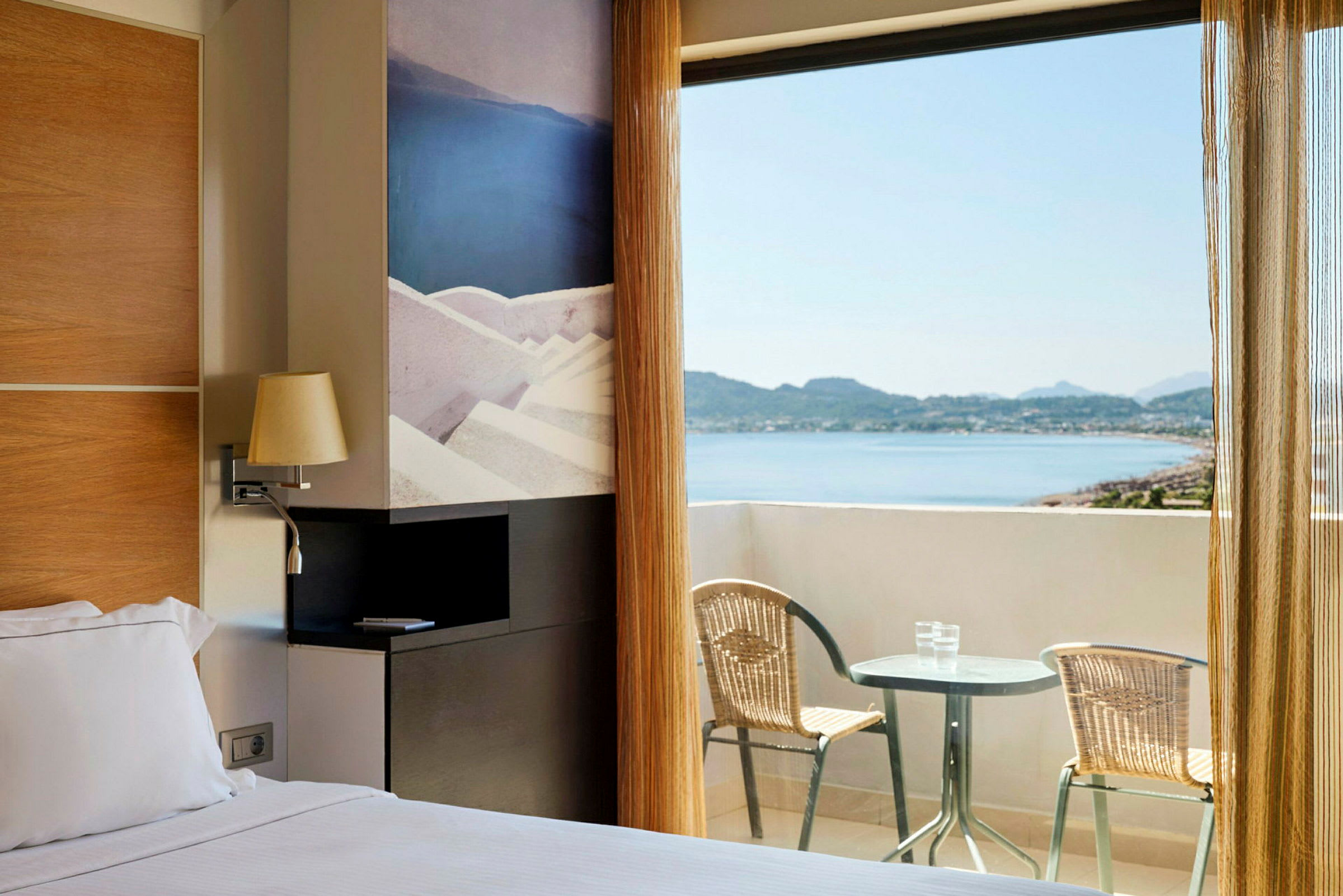 Hotellrom med dobbeltseng og utgang til en balkong med utsikt over havet. (AI-generert tekst)