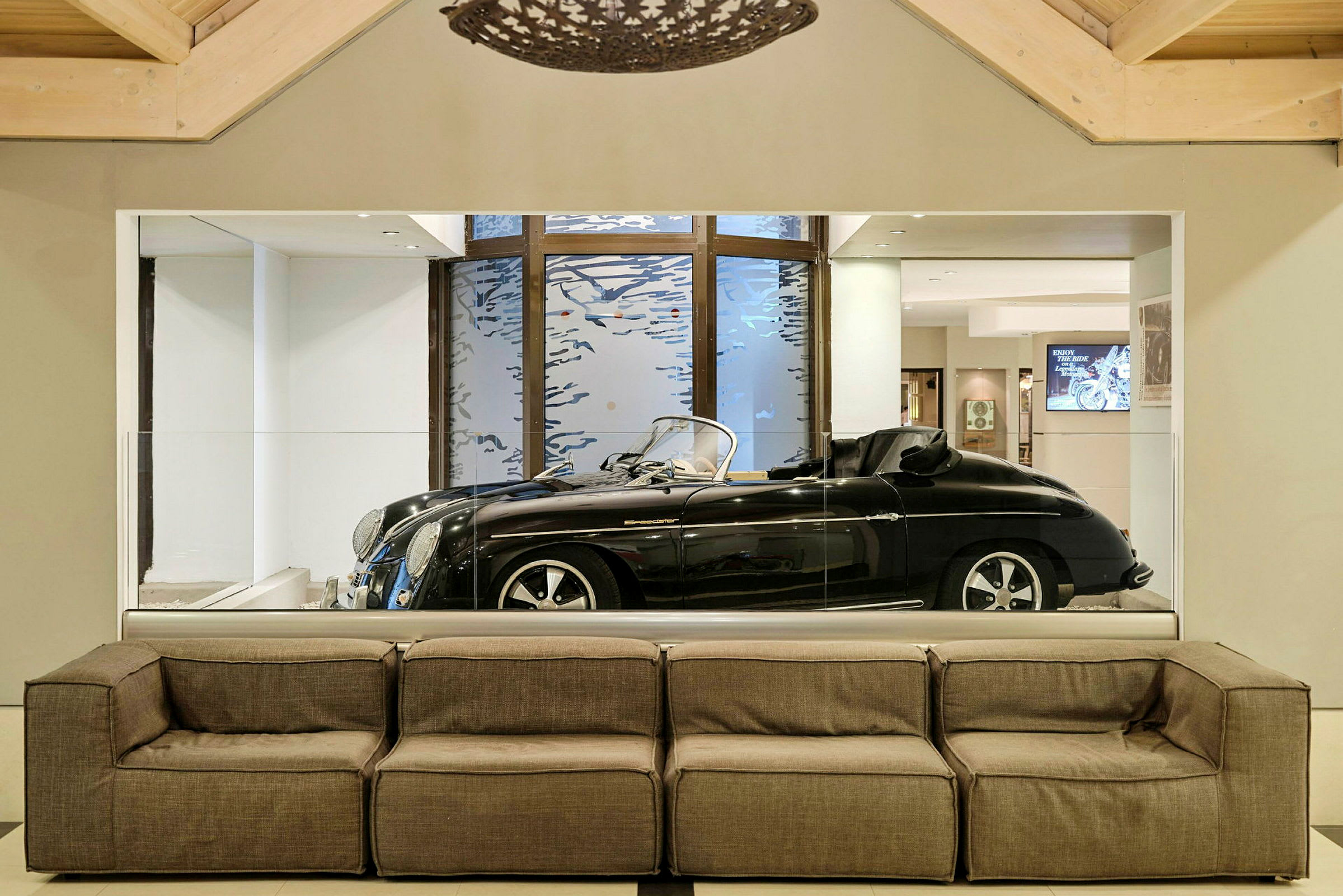 En svart sportsbil bak glassvegg i et moderne rom med grå sofa. (AI-generert tekst)