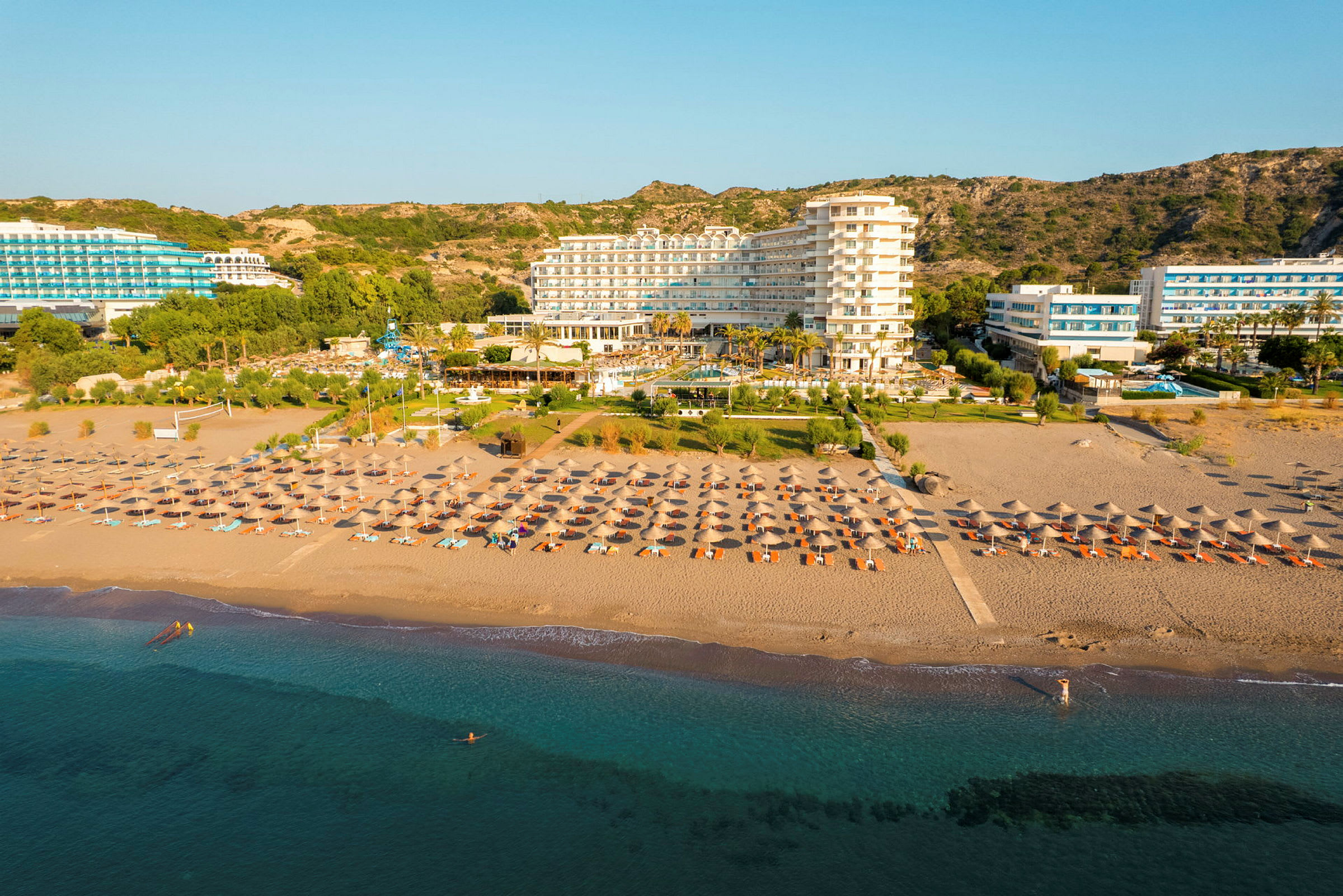 Et hotell ved stranden med solsenger og parasoller foran og en klar blå himmel i bakgrunnen. (AI-generert tekst)