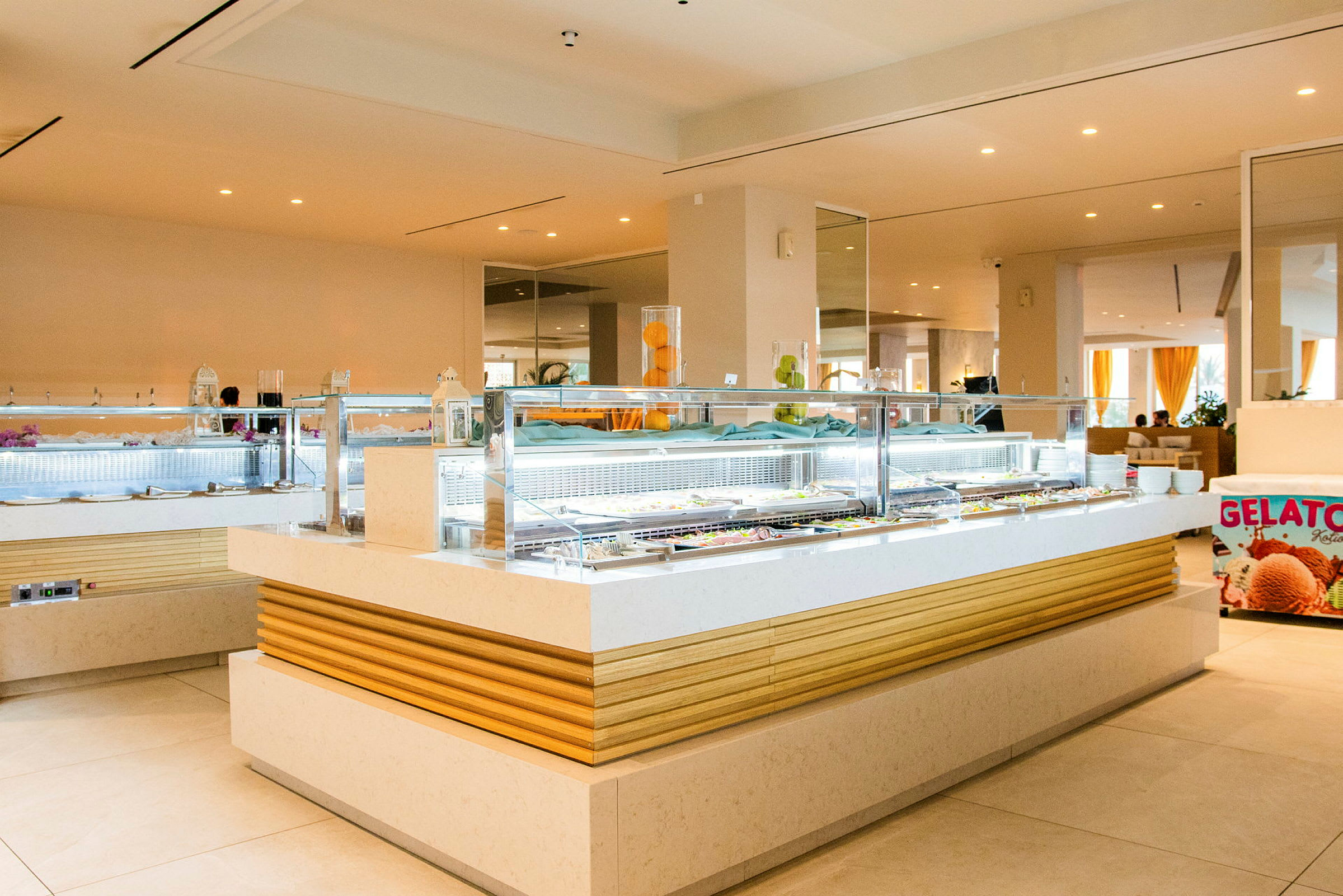 Et bilde av en moderne bufféstasjon med et is-skilt som viser "Gelato" og en glassdisk med forskjellige matalternativer. (AI-generert tekst)