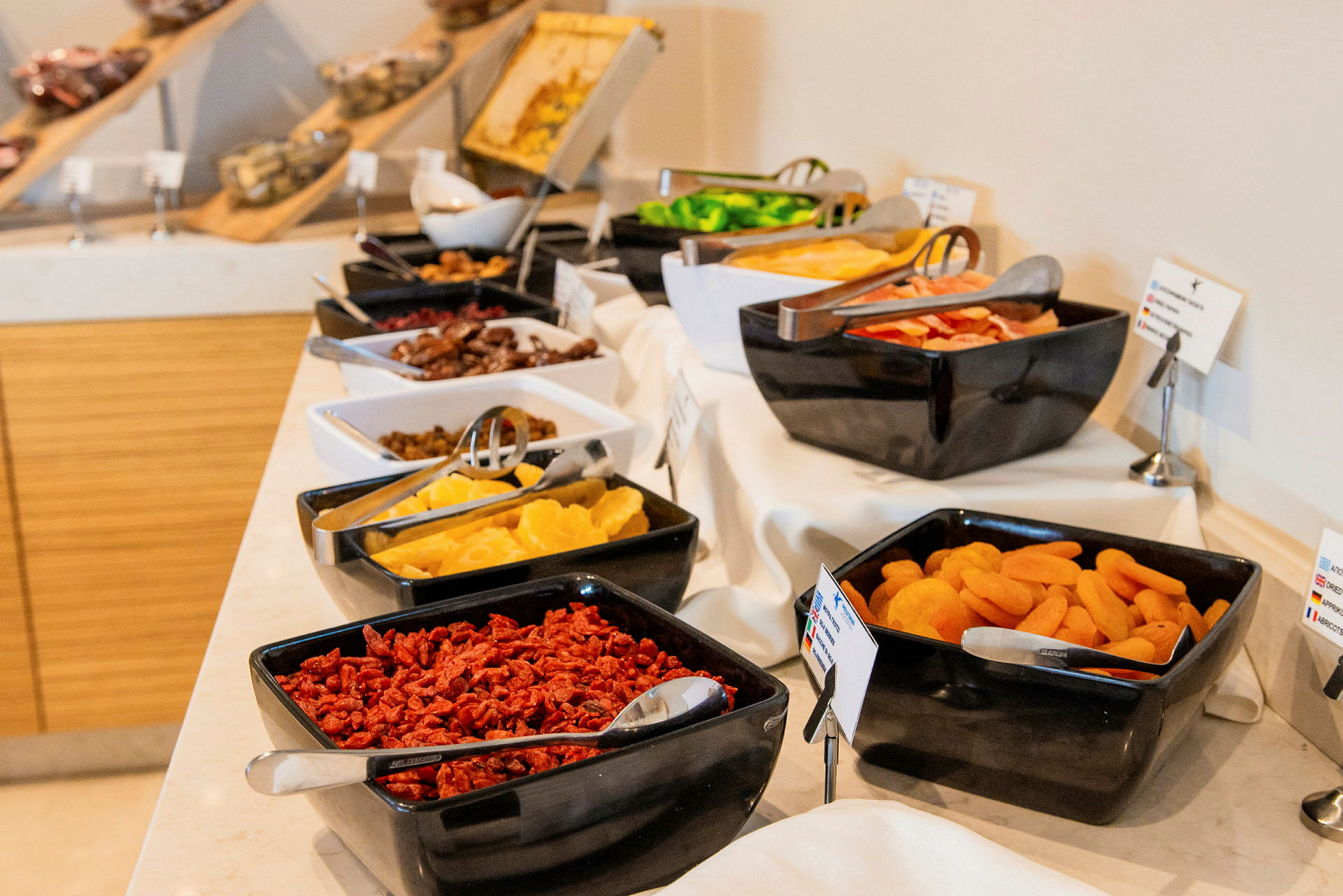 En buffet med forskjellige tørkede frukter og ferske matvarer i svarte og hvite skåler på et dekket bord. (AI-generert tekst)