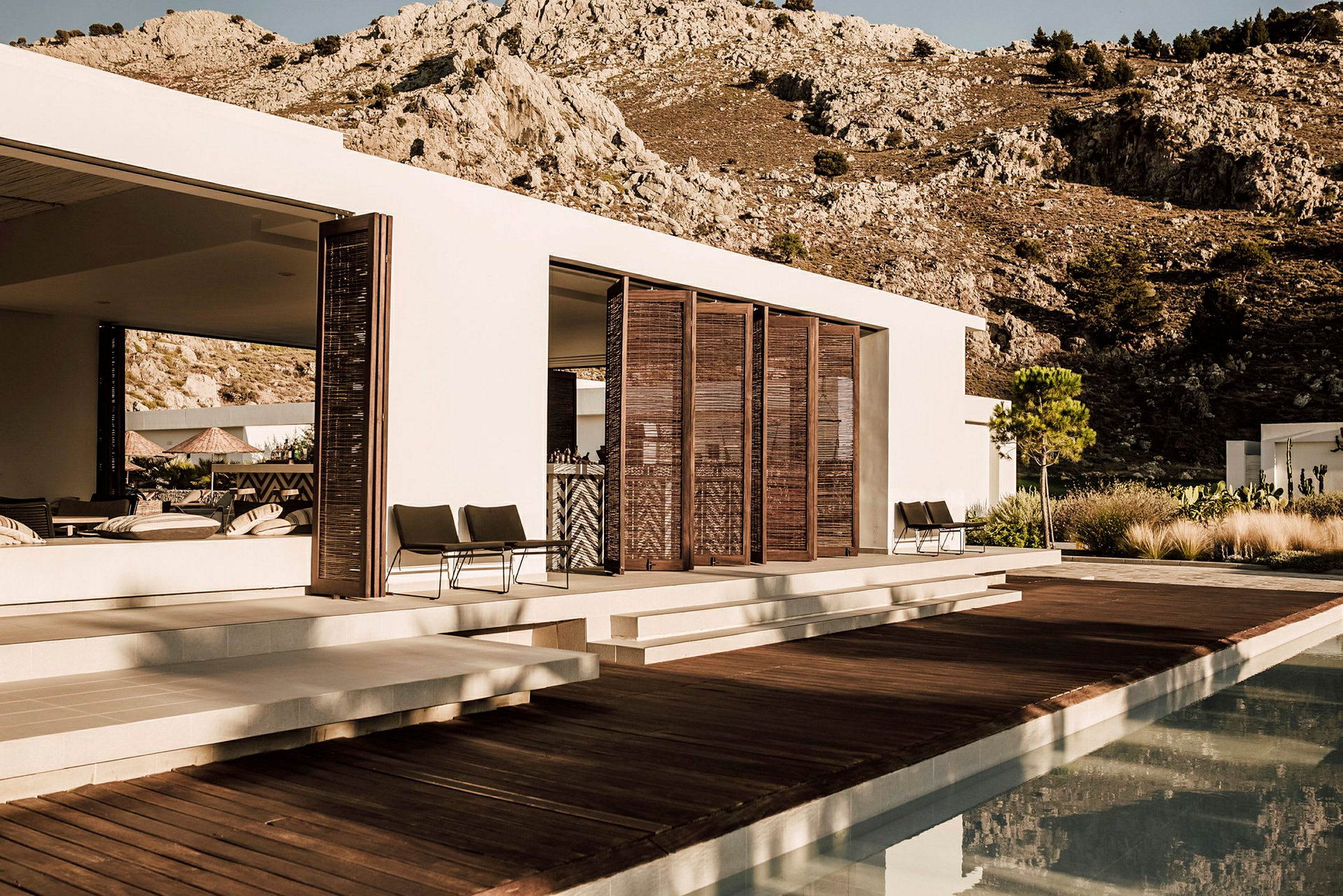 Moderne villa med treterrasse og basseng foran fjellandskap. (AI-generert tekst)