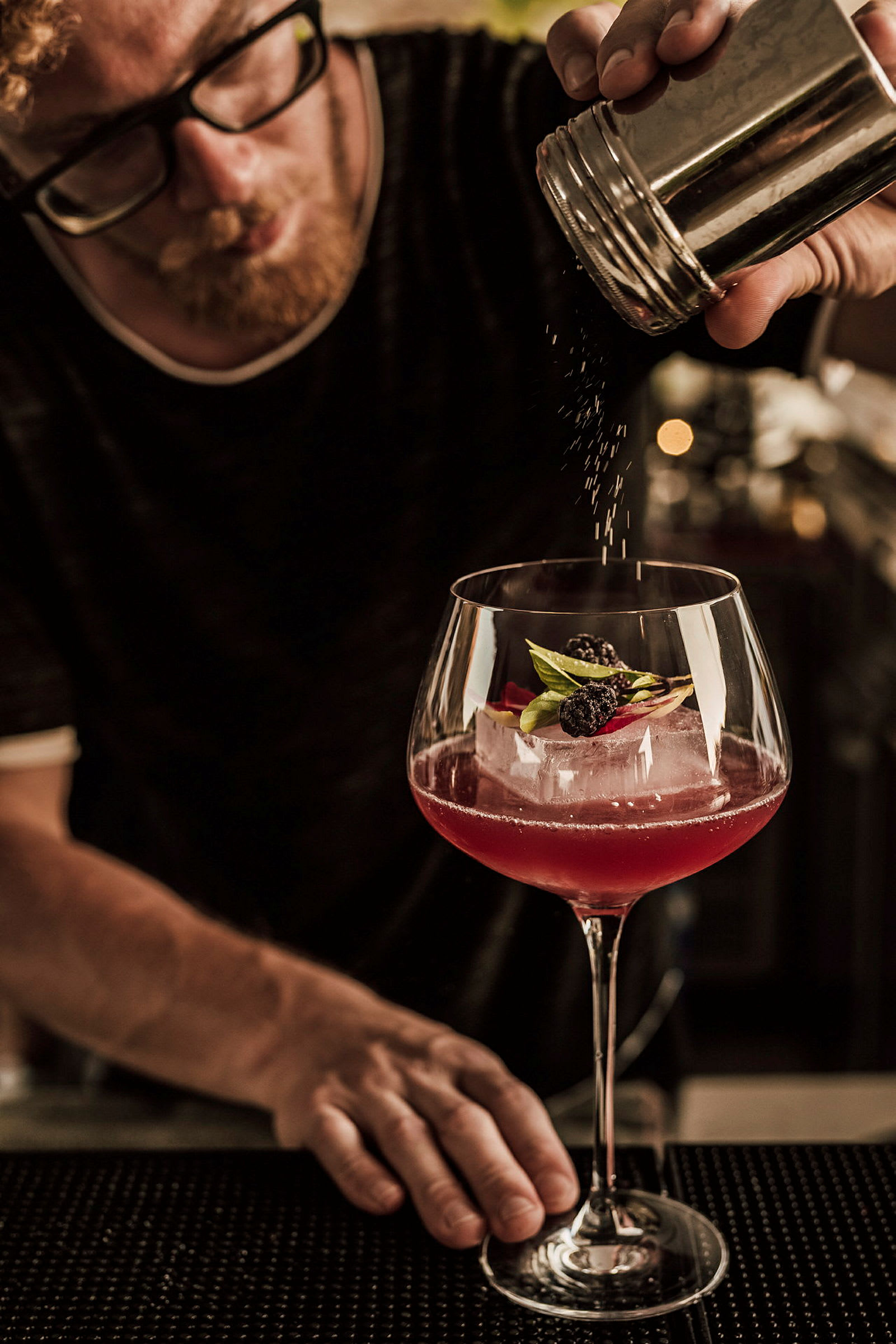 En hånd strør pulver over en cocktail pyntet med bær og blader. (AI-generert tekst)