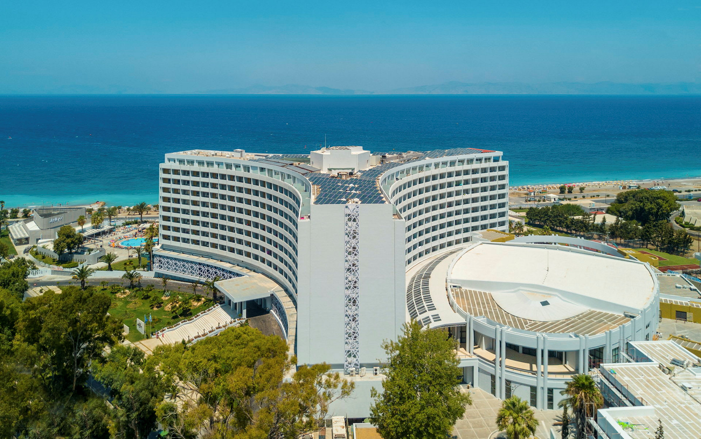 Hotellet med havet og stranden i bakgrunnen. (AI-generert tekst)