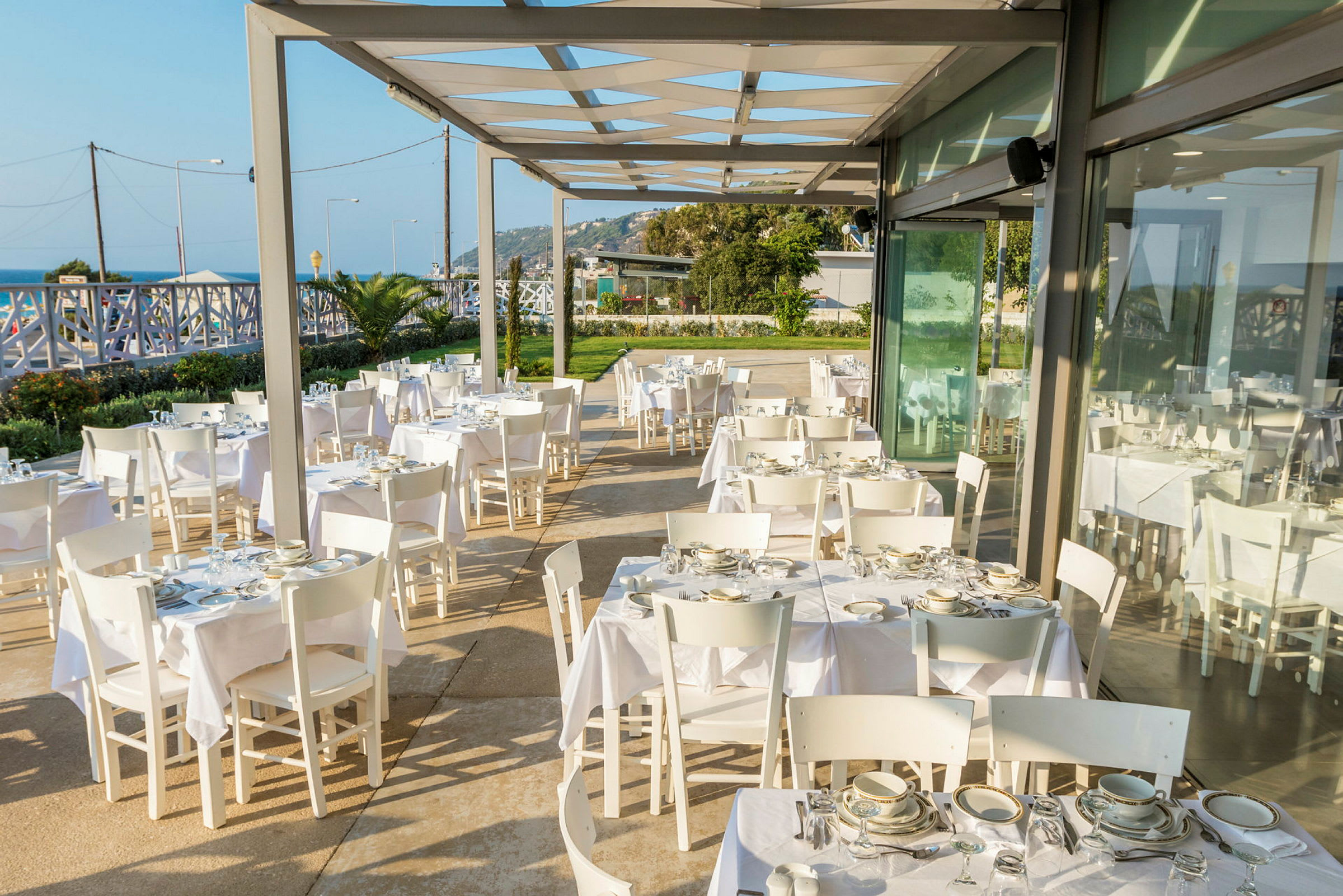 Utendørsrestaurant med hvite bord og stoler samt tallerkener og glass. (AI-generert tekst)