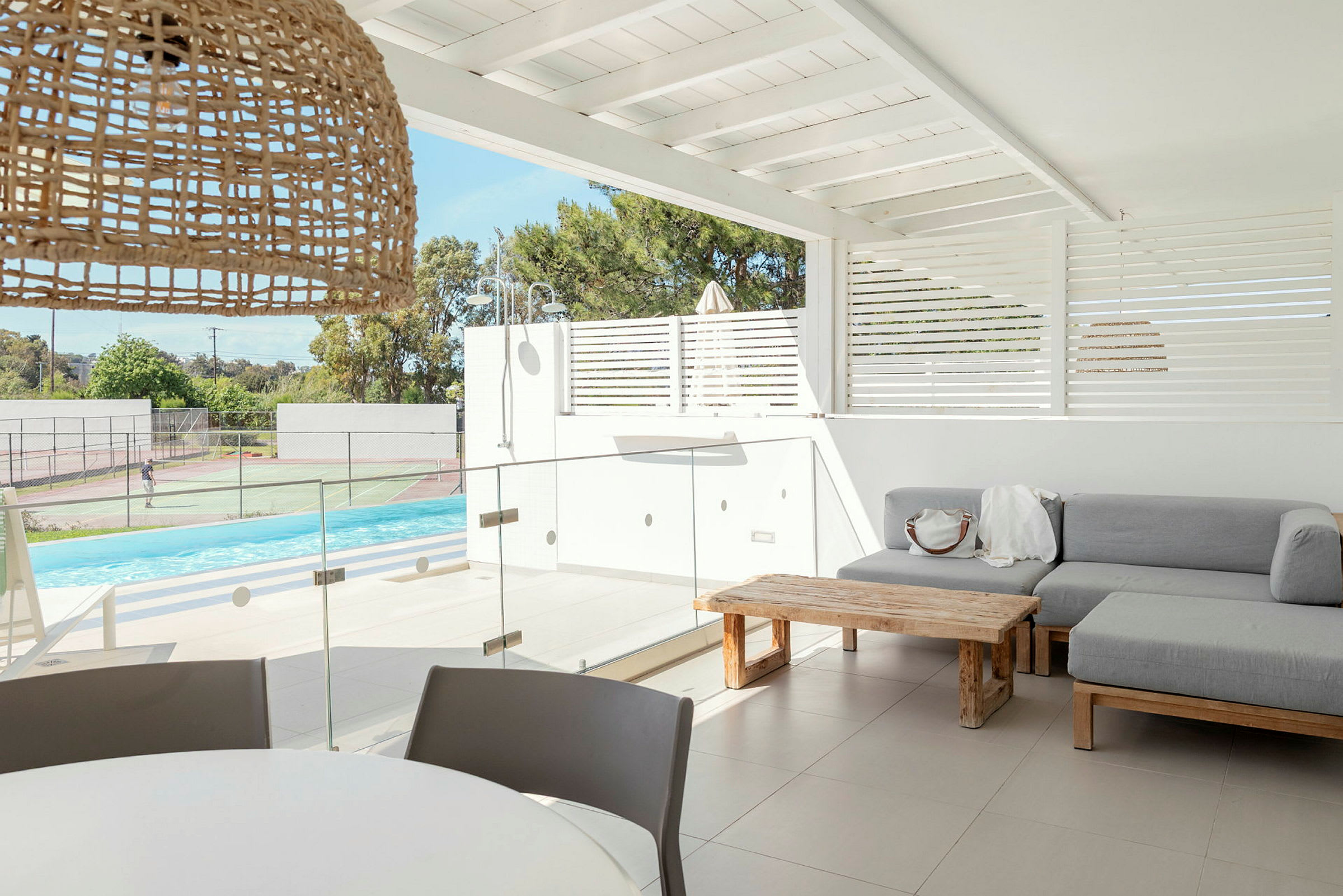 En moderne uteplass med sofa, bord og utsikt over basseng og tennisbaner. (AI-generert tekst)