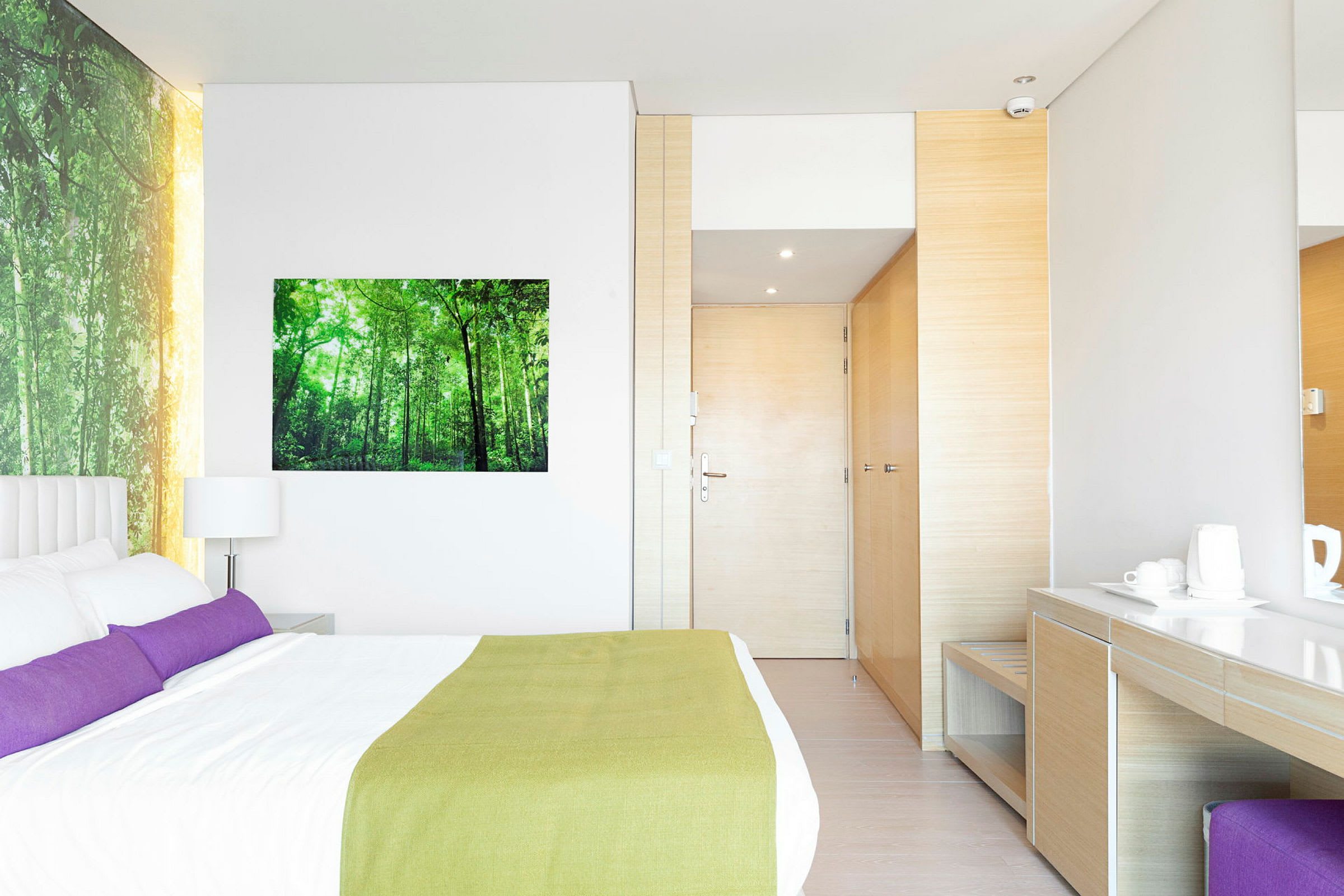 Bilde av et moderne hotellrom med en dobbeltseng, skrivebord og garderobe. Veggen er dekorert med et naturbilde. (AI-generert tekst)