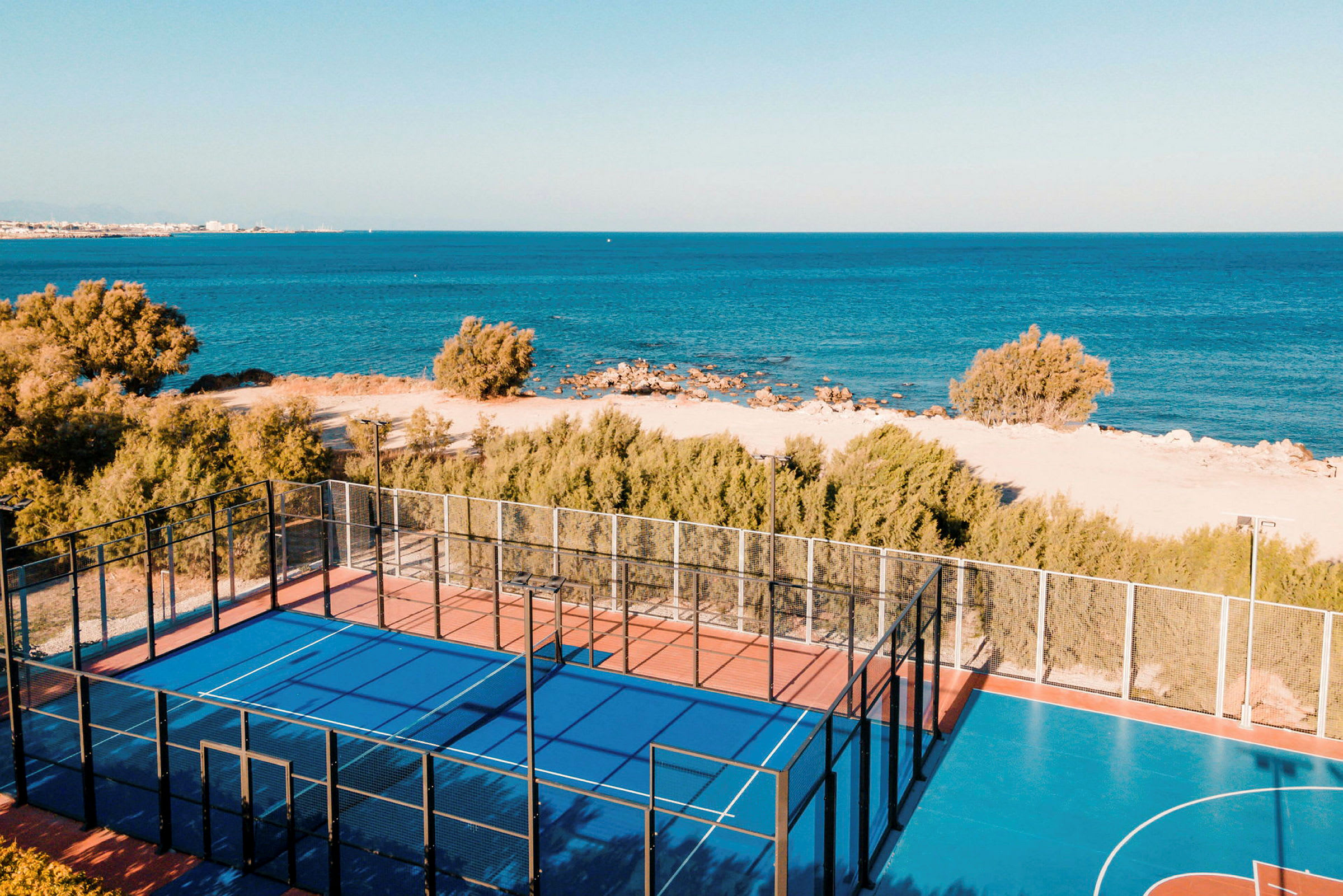 Padelbane med blått dekke nær stranden og sjøen. (AI-generert tekst)