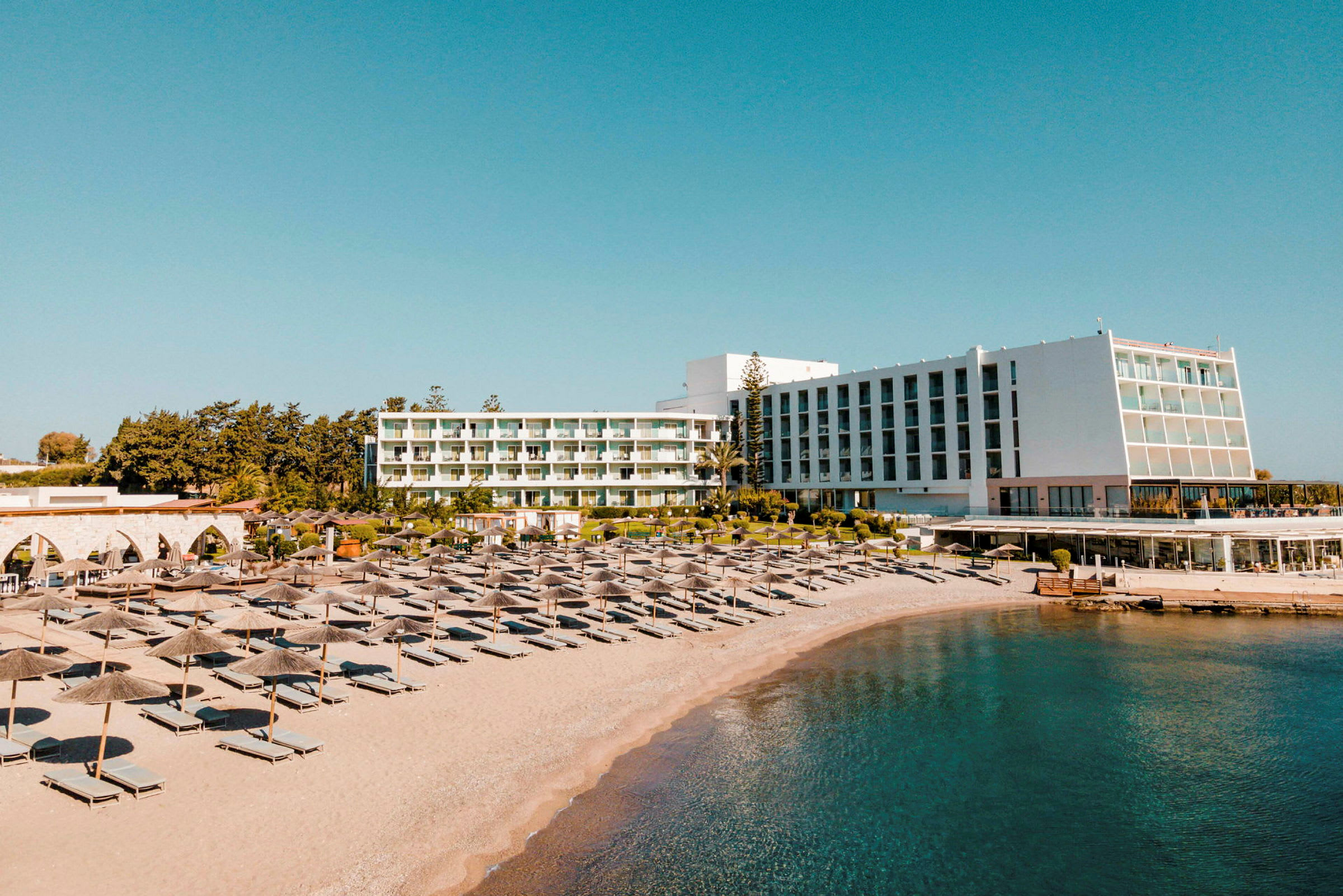 Utsikt over hotellet og stranden med solsenger og parasoller. (AI-generert tekst)