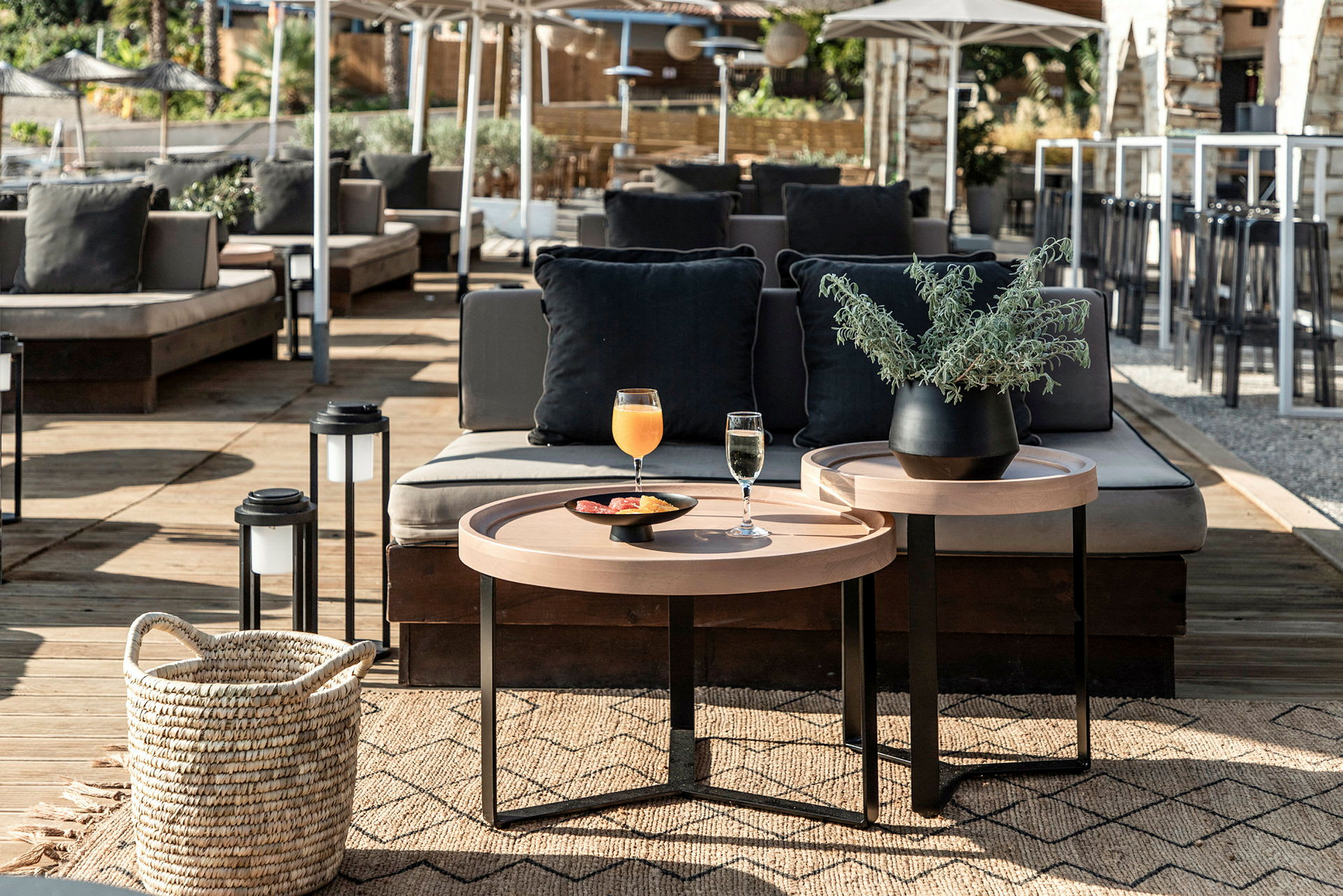 En utendørs terrasse med sofaer, et bord med drikker og en plante i potte. (AI-generert tekst)