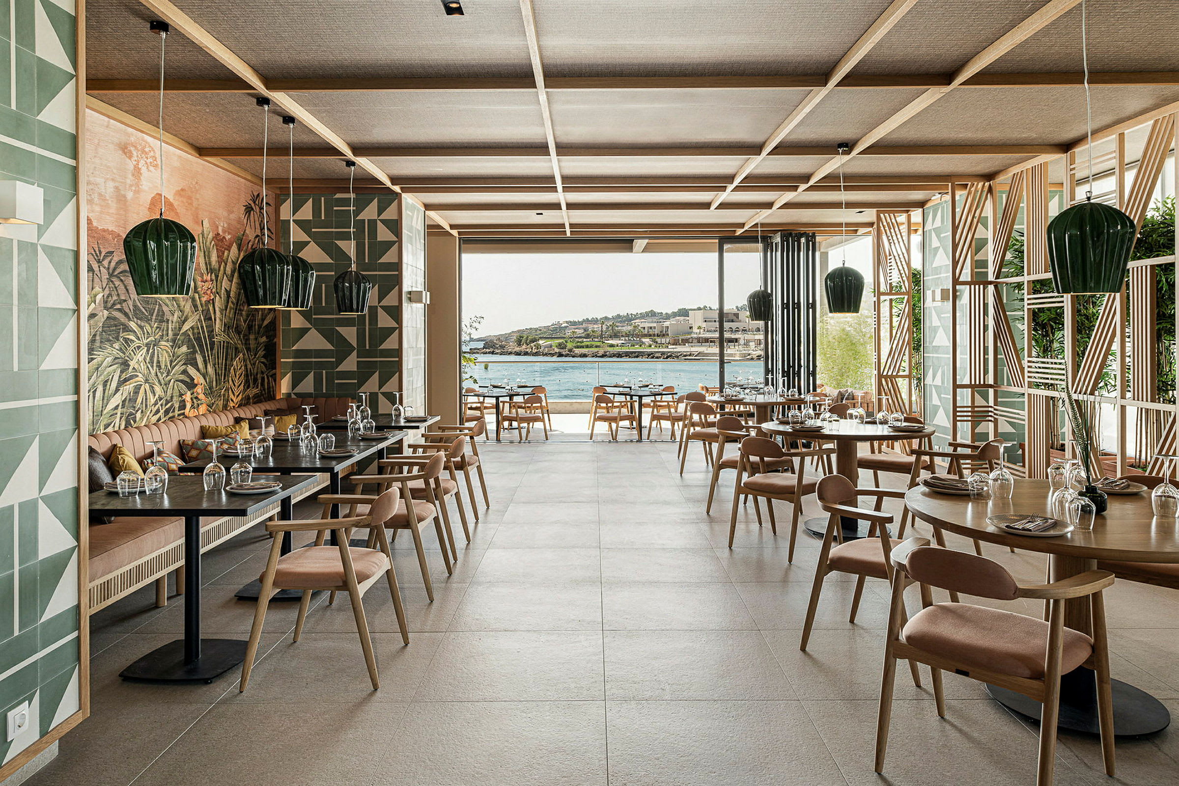 Interiør av en restaurant med bord og stoler, stor glassåpning og utsikt over vannet. (AI-generert tekst)
