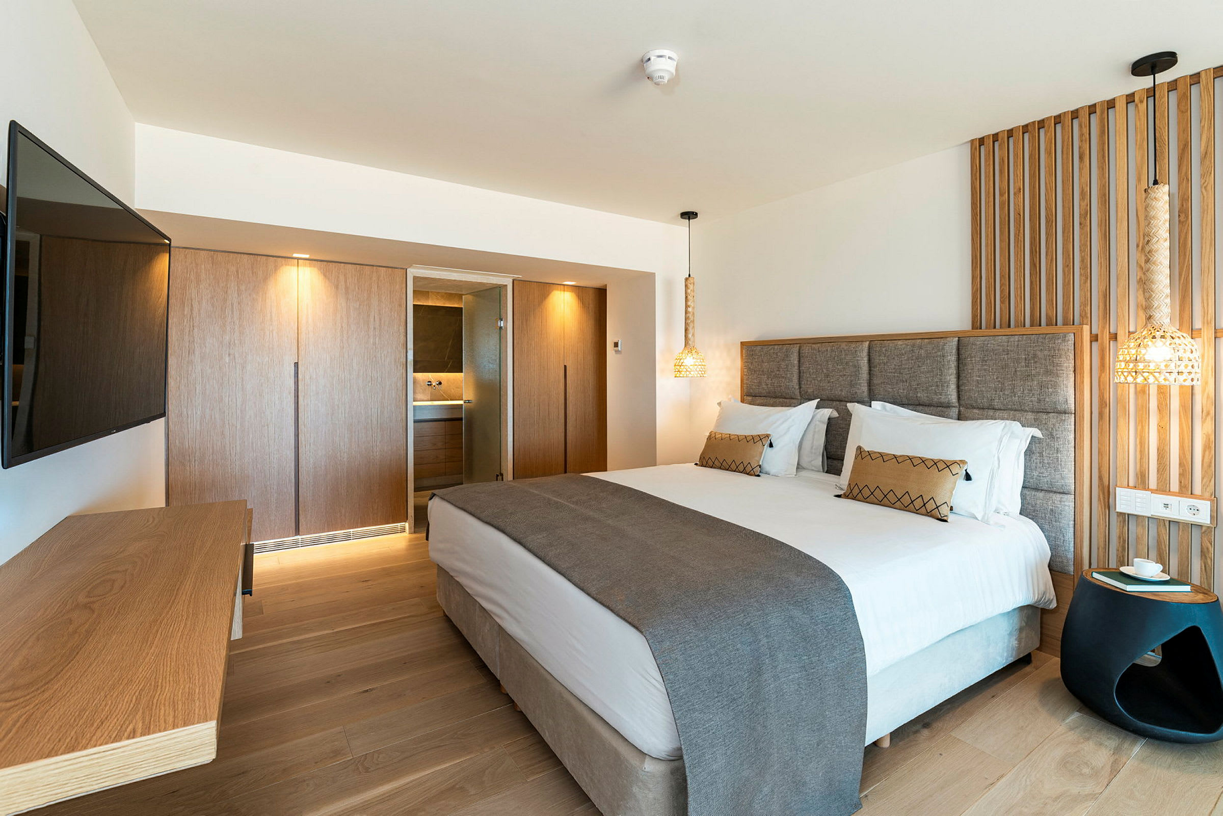 Et moderne hotellrom med en dobbeltseng, en veggmontert TV, en trepanel bak sengen og et skrivebord. (AI-generert tekst)