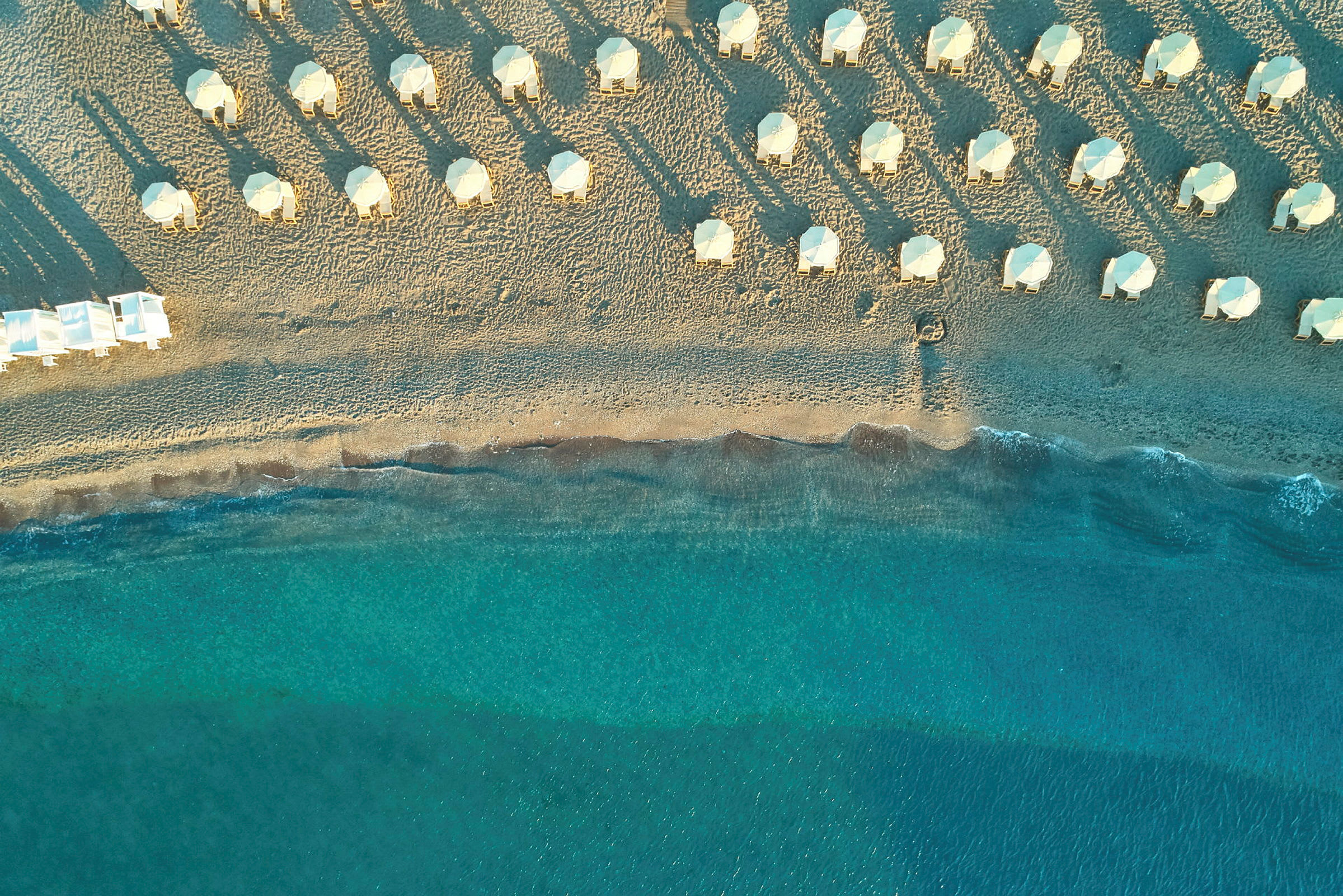 Flyfoto av en strand med parasoller og solsenger, samt klart blått hav. (AI-generert tekst)