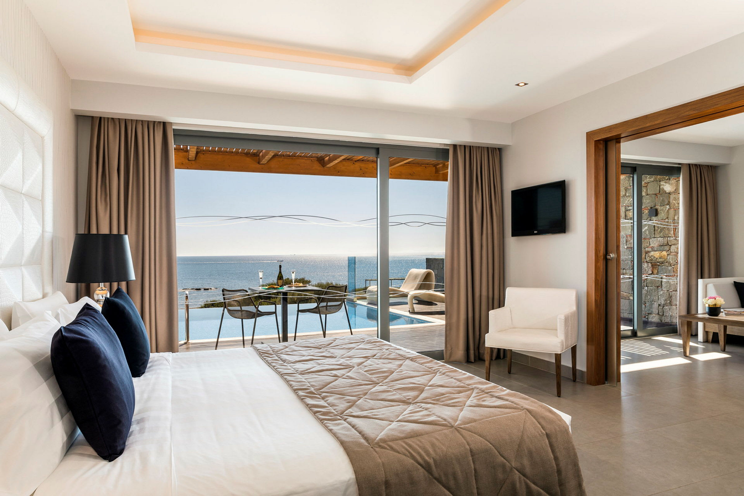 Et hotellrom med stor seng og utsikt mot havet fra en glassfasade. (AI-generert tekst)