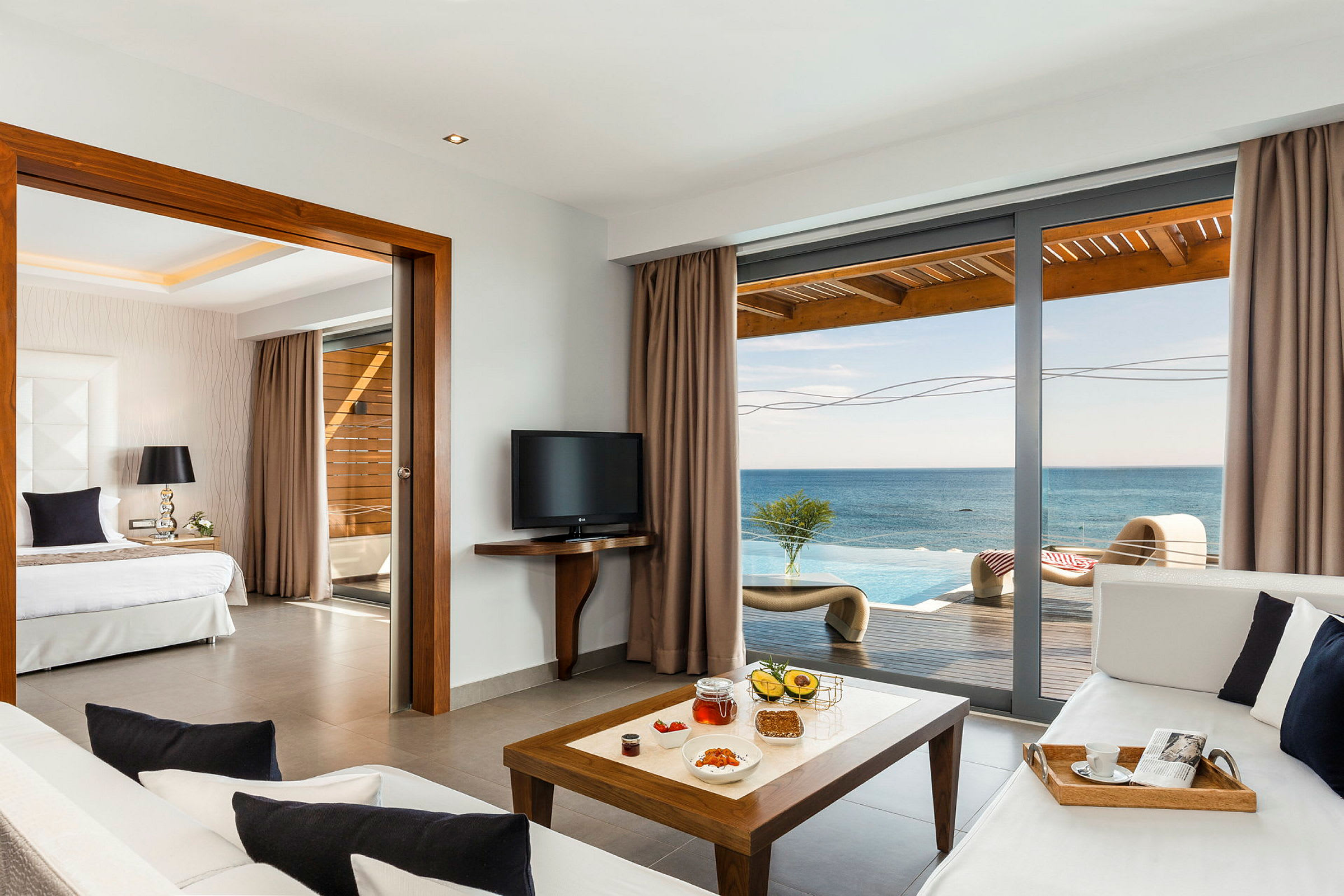Et moderne hotellrom med havutsikt gjennom store glassdører, oppholds- og sovedel. (AI-generert tekst)