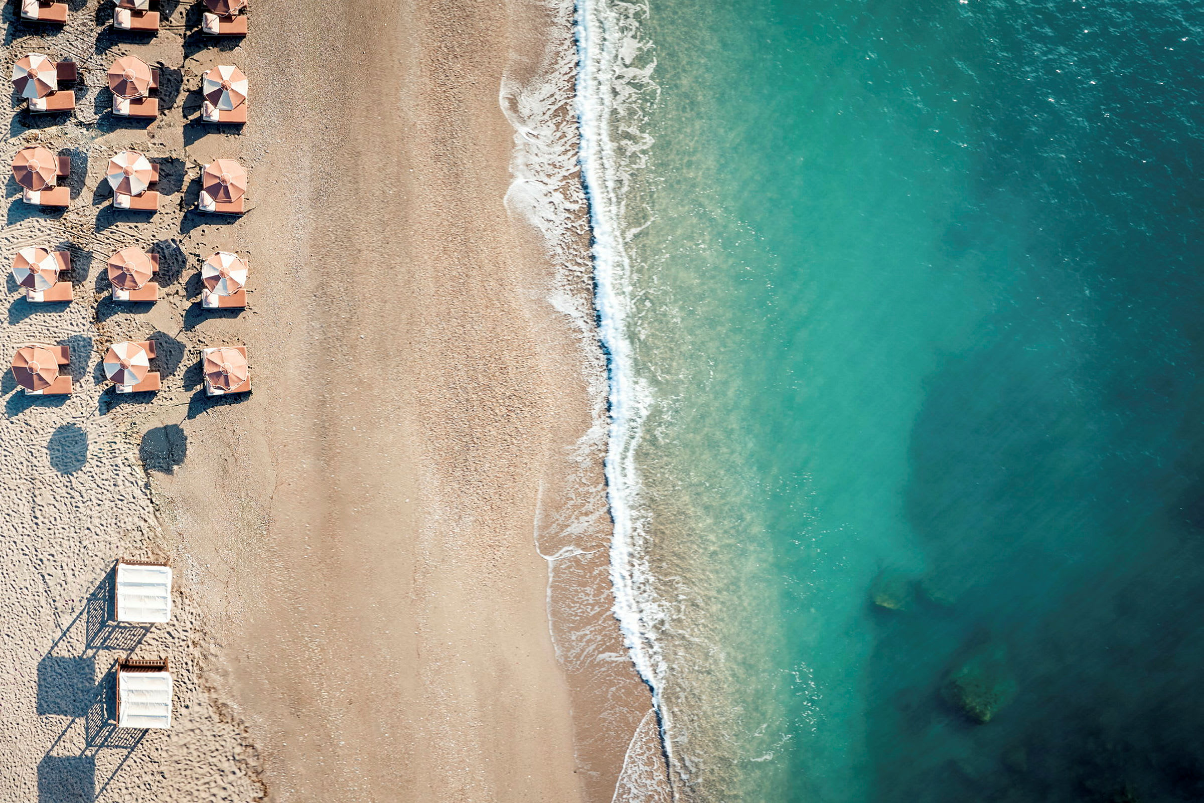 Luftfoto av en strand med parasoller og turkist vann. (AI-generert tekst)