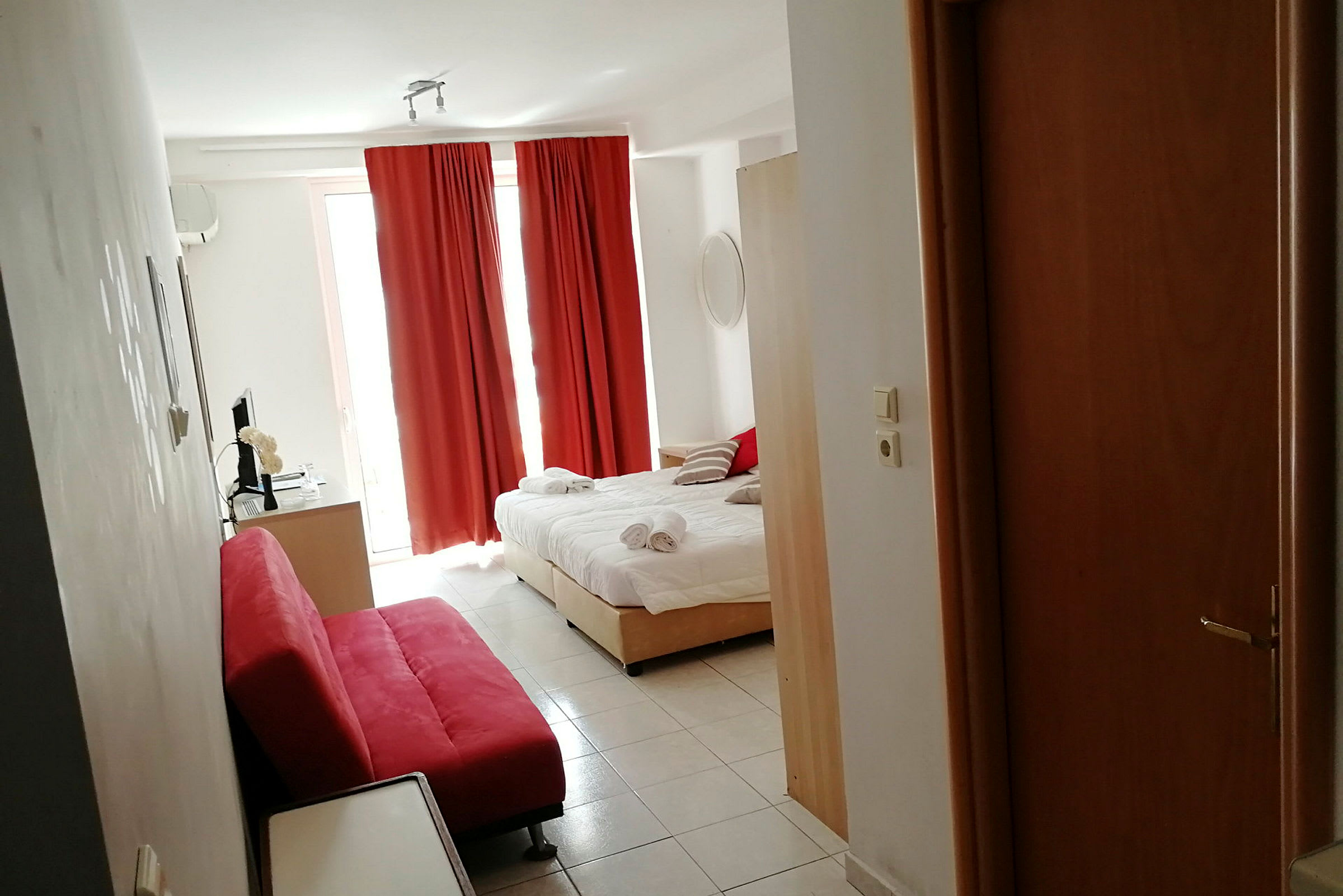 Et hotellrom med en oppredt seng, røde gardiner og en rød sofa. (AI-generert tekst)