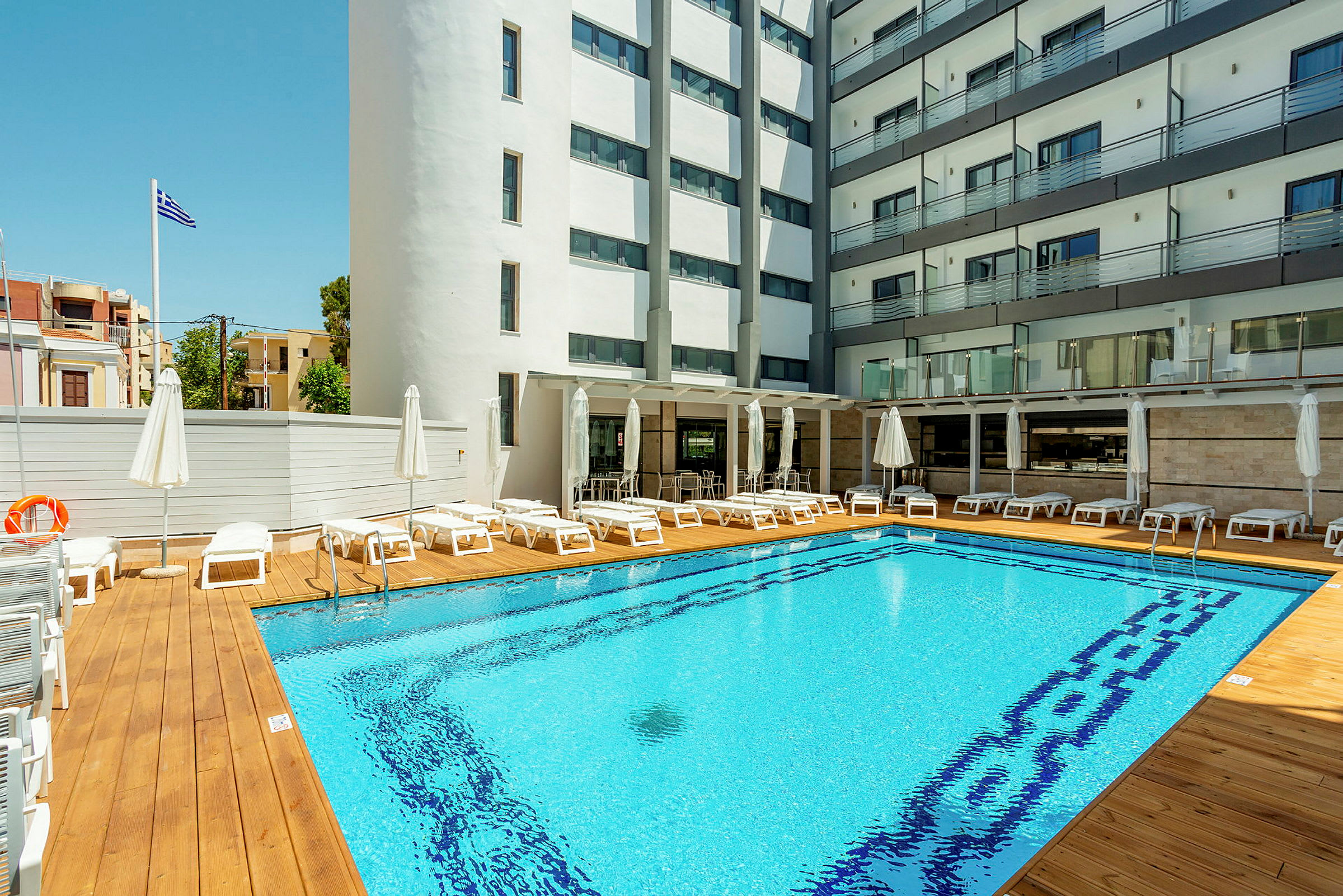 Hotellbasseng med solsenger og parasoller, omgitt av bygninger. (AI-generert tekst)