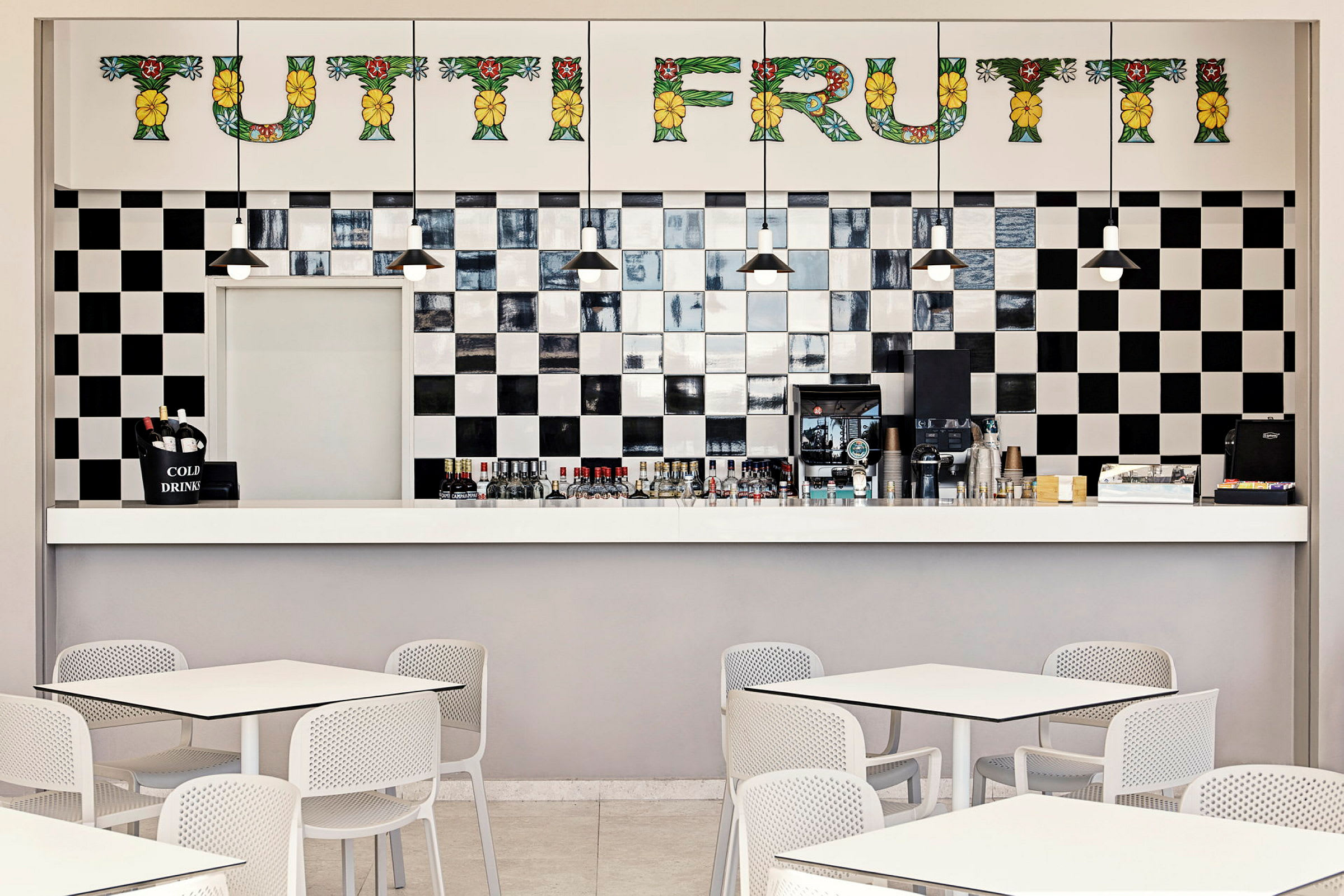 Bilde av en kafé med en svart-hvitt flislagt vegg og sitteplasser med hvite bord og stoler. (AI-generert tekst)