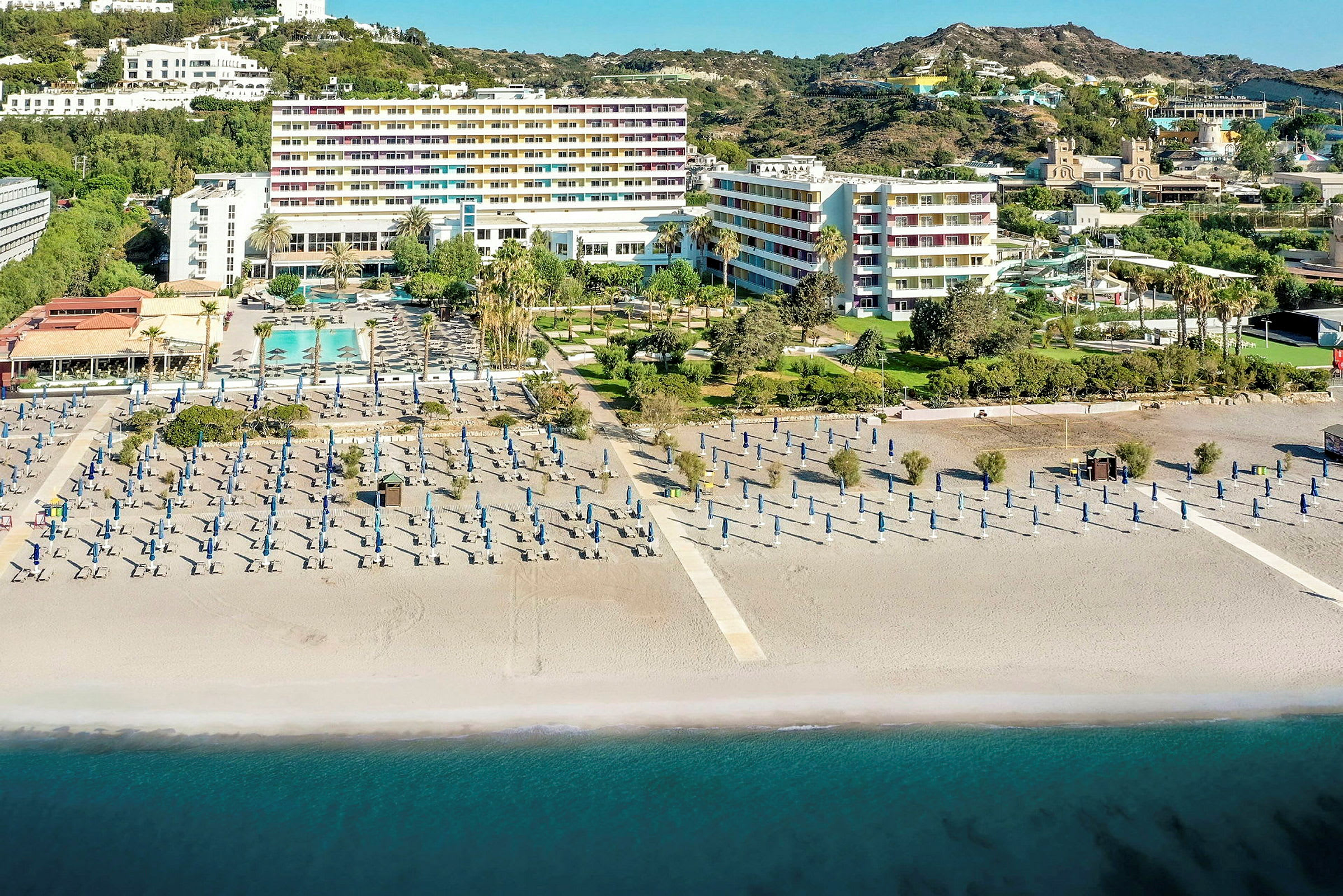 Hotellkompleks ved stranden med solsenger og parasoller, og havet i forgrunnen. (AI-generert tekst)