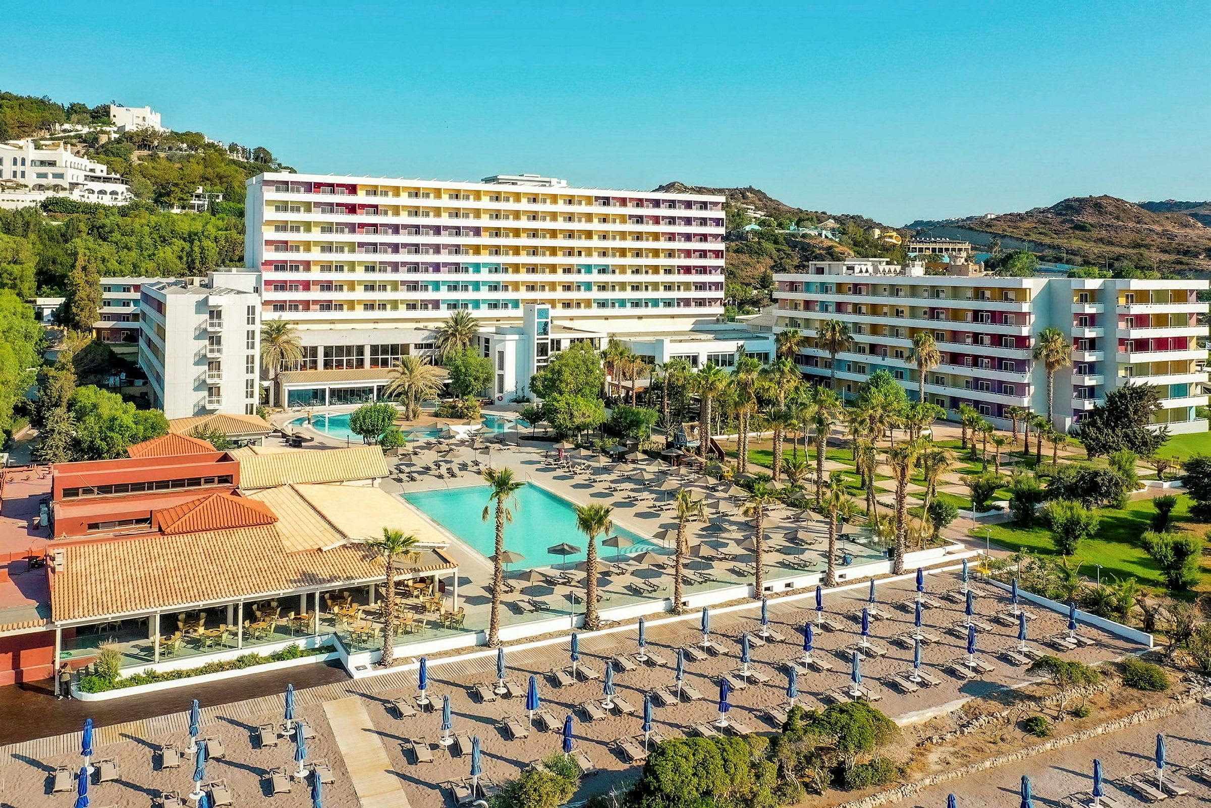 Hotellområde med basseng, solsenger og sandstrand i bakgrunnen. (AI-generert tekst)